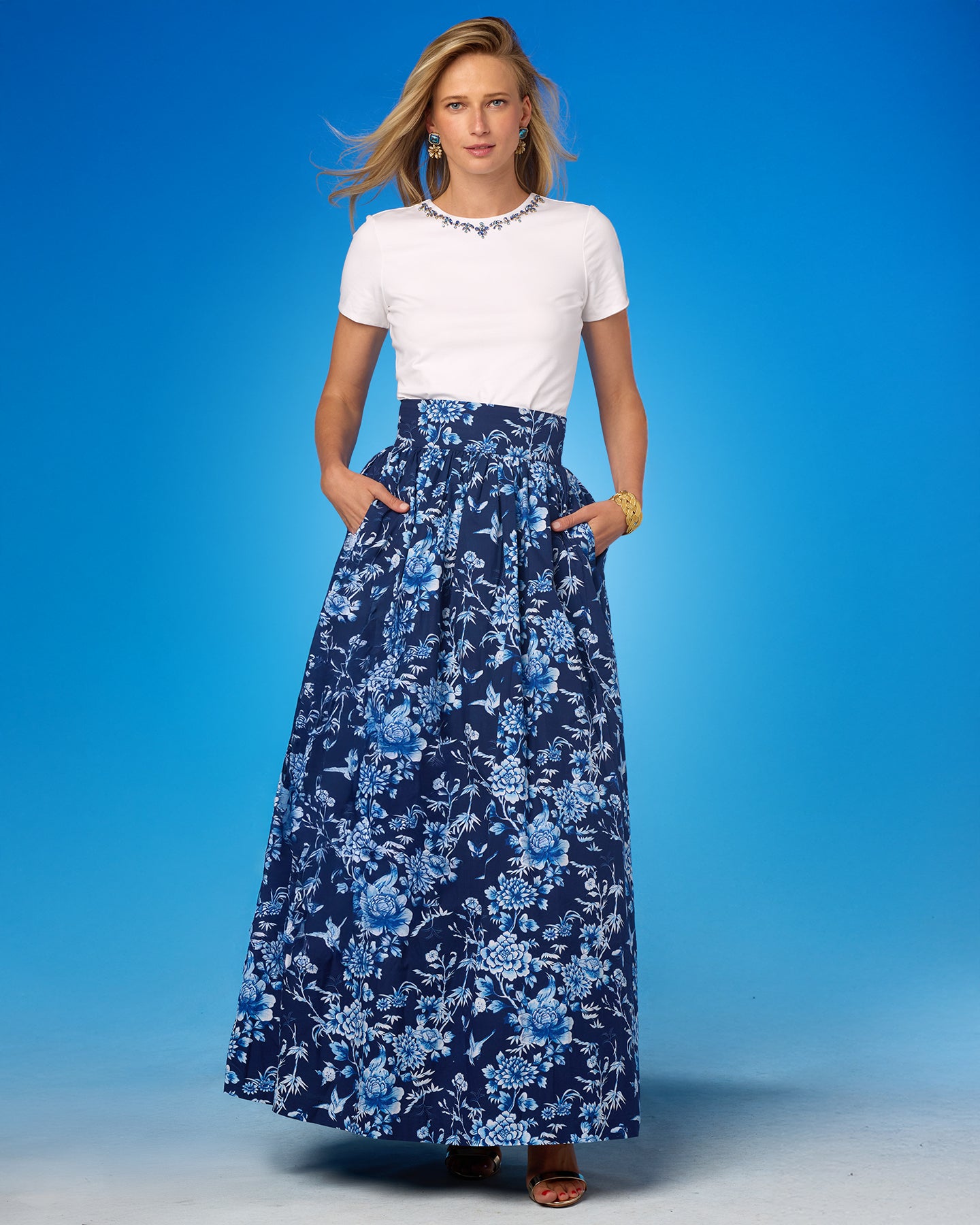 Woman wearing a white top and blue floral skirt against a blue background