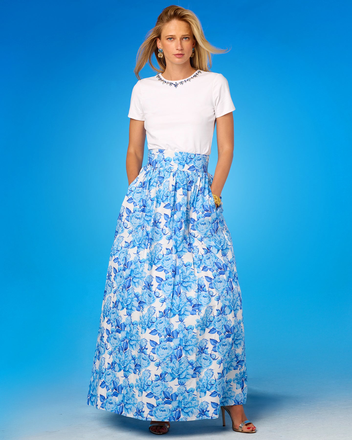 Woman wearing a white top and blue floral skirt against a blue background