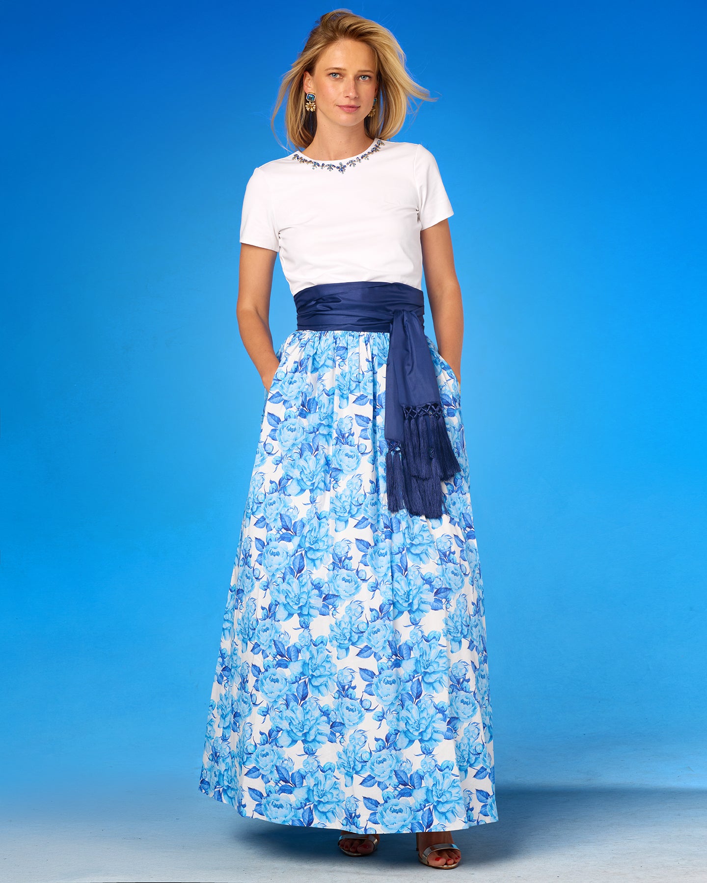 Woman wearing a long blue floral skirt with a white top against a blue background