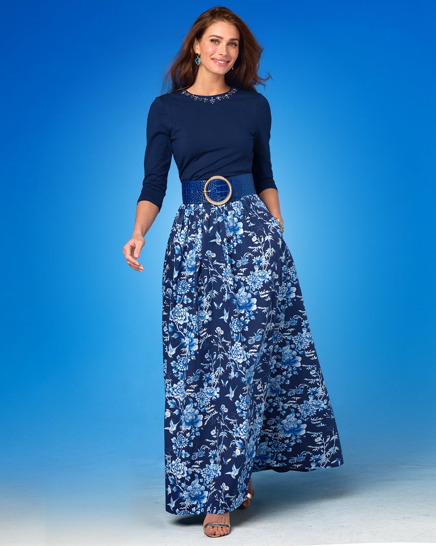 Woman wearing a navy top and blue floral skirt against a blue background