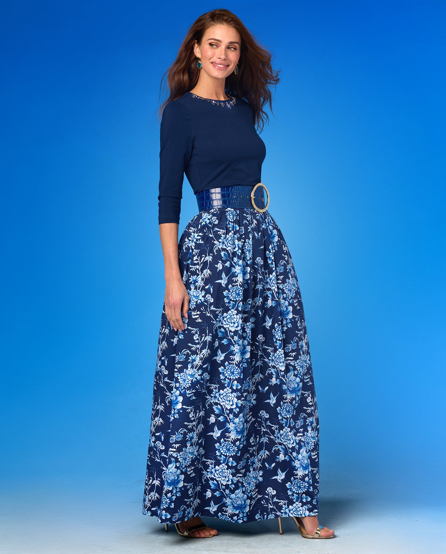Woman wearing a navy blue top and floral skirt against a blue background