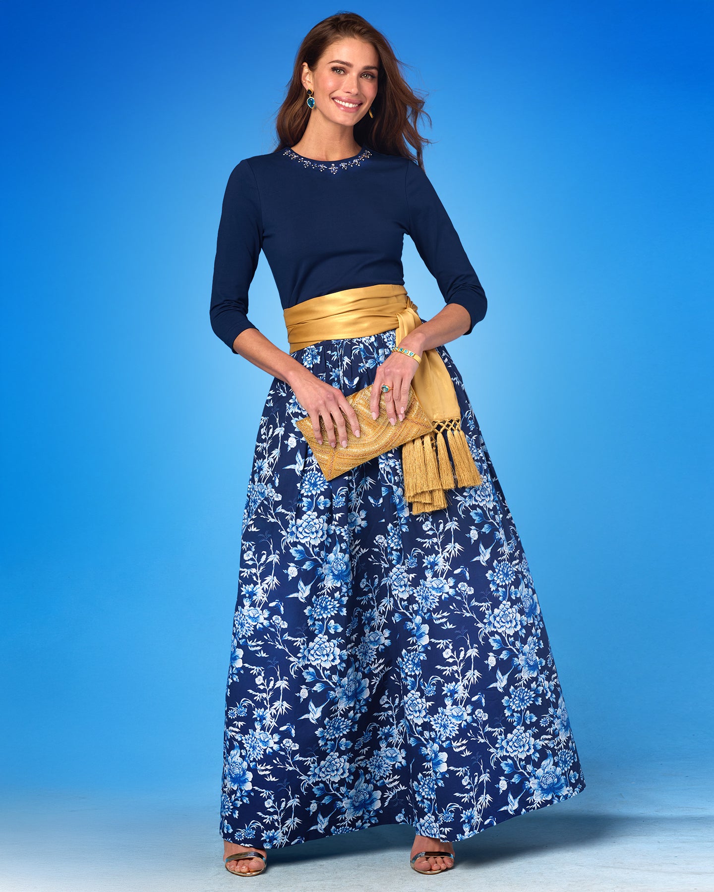 Woman wearing a navy top and floral skirt with a yellow belt against a blue background
