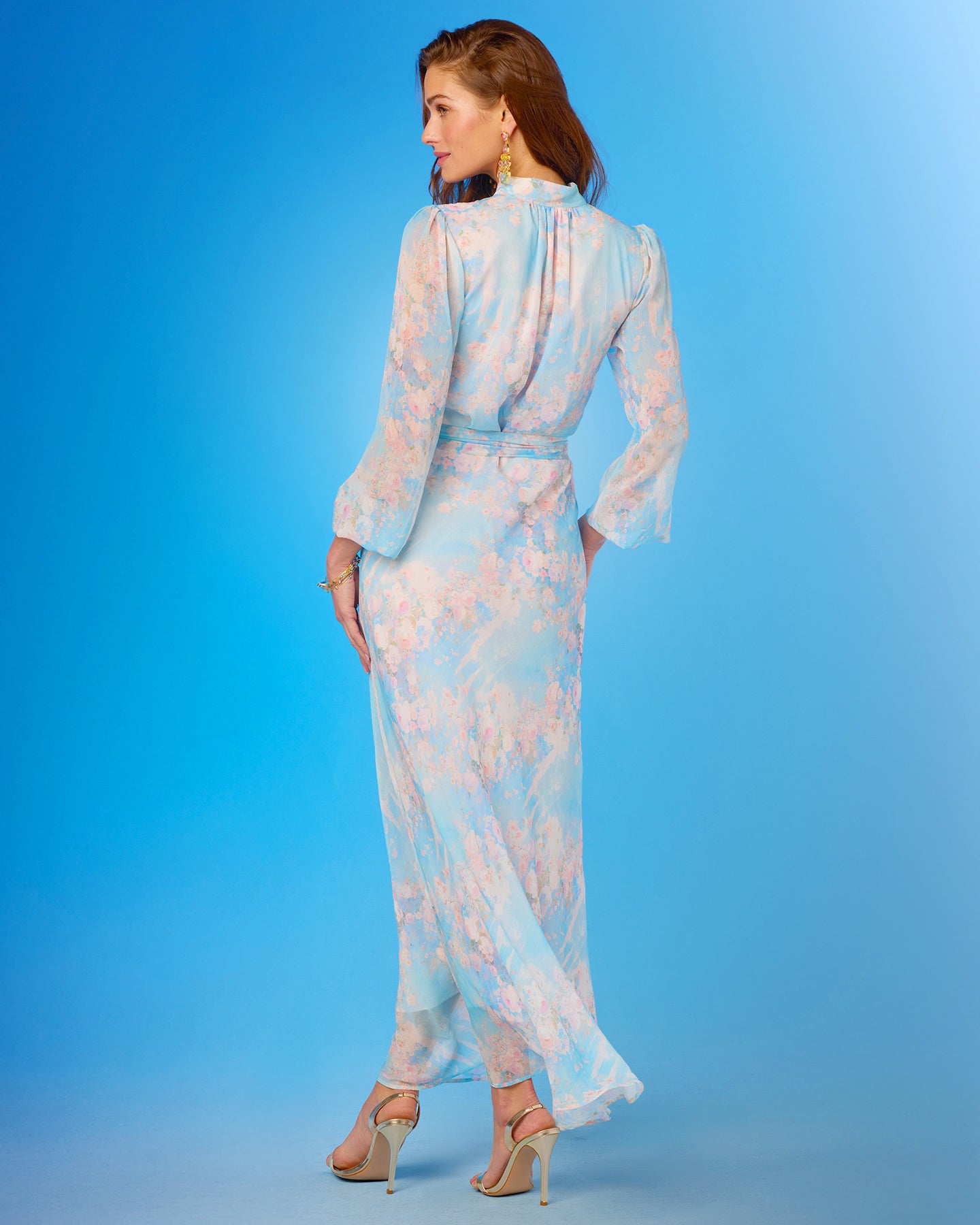 Woman wearing a light blue floral dress viewed from the back against a blue background