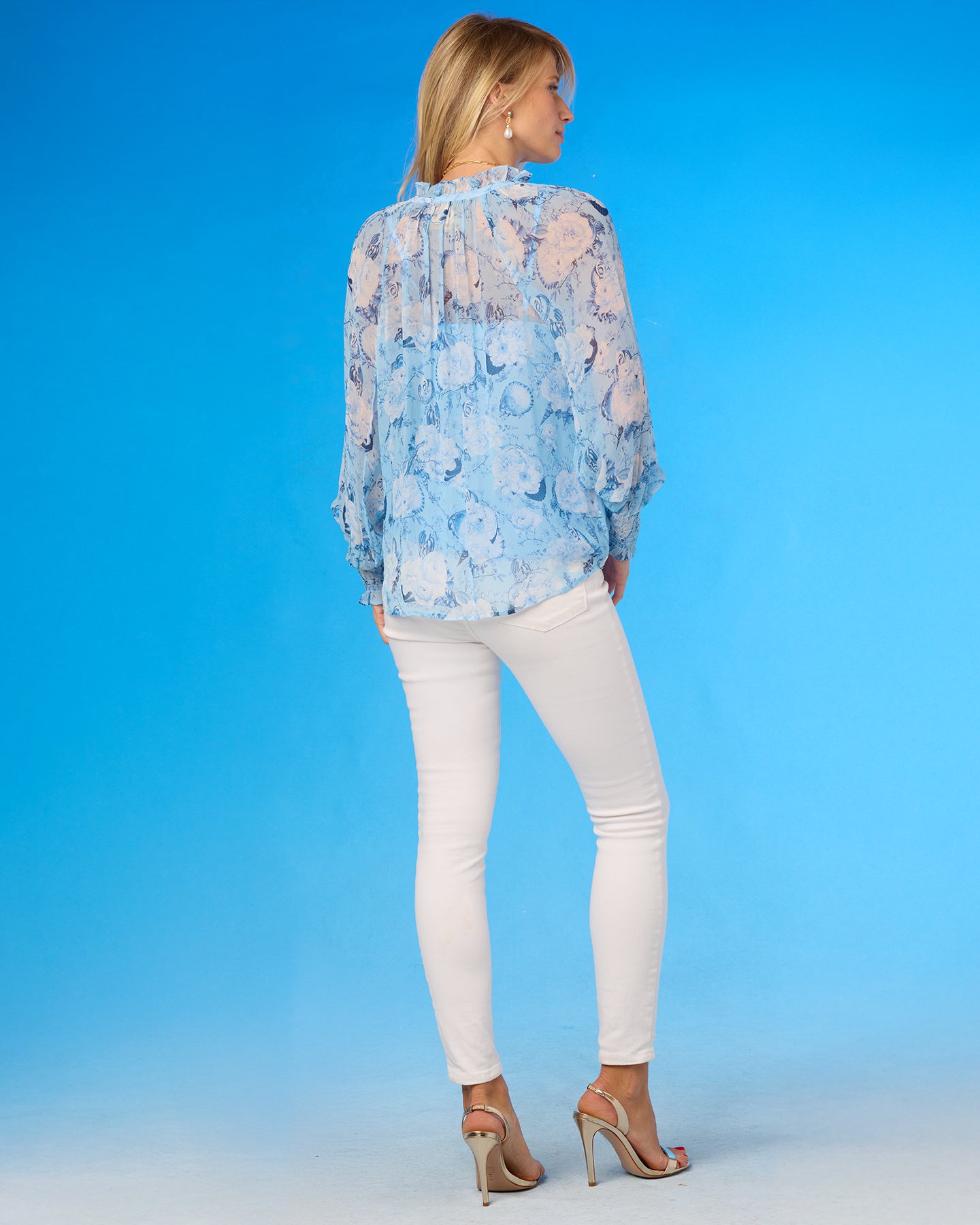 Woman wearing a light blue floral blouse and white pants against a blue background