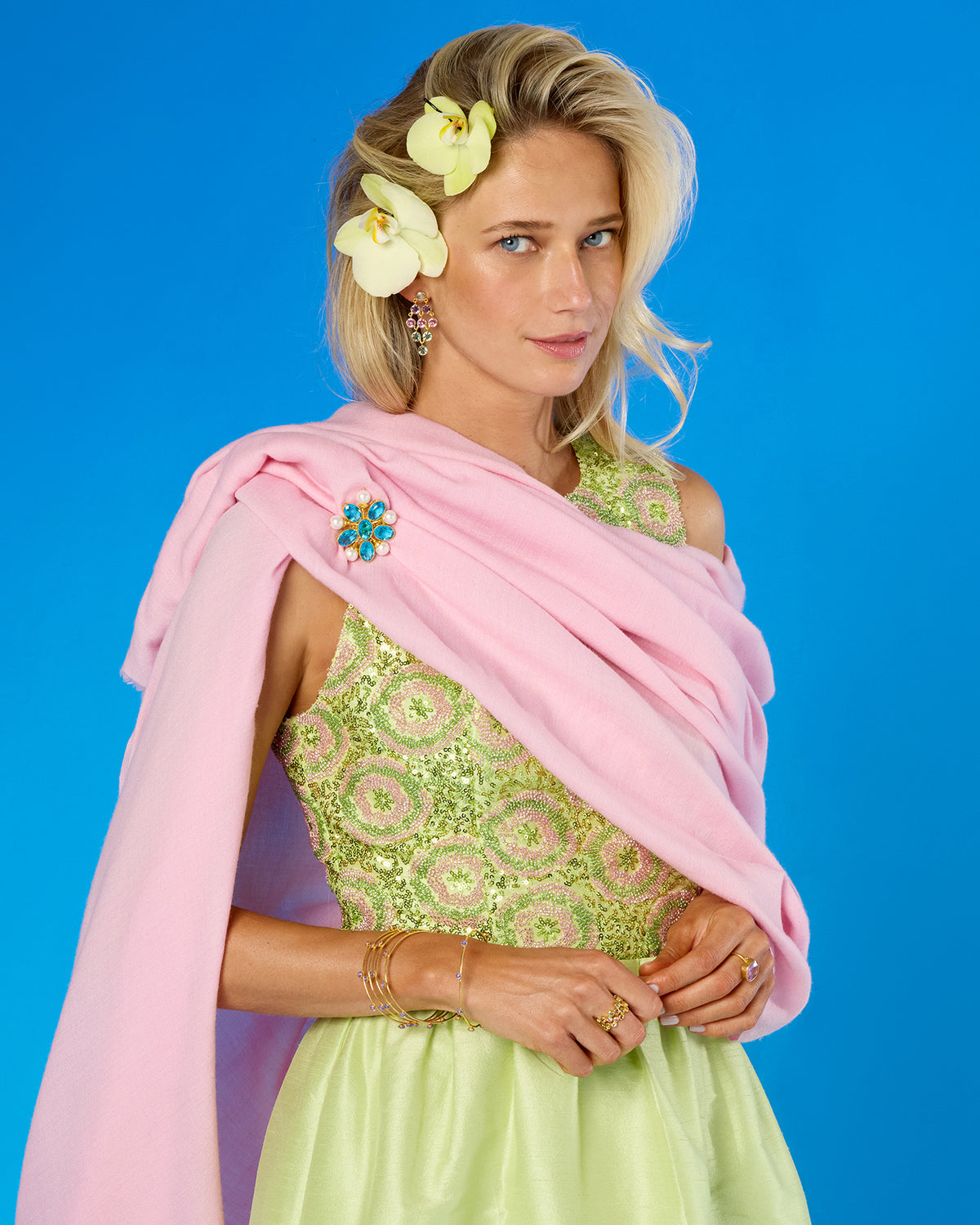 A woman models a light pink dupatta draped over her shoulders, paired with a light green embroidered dress, set against a solid blue studio background.