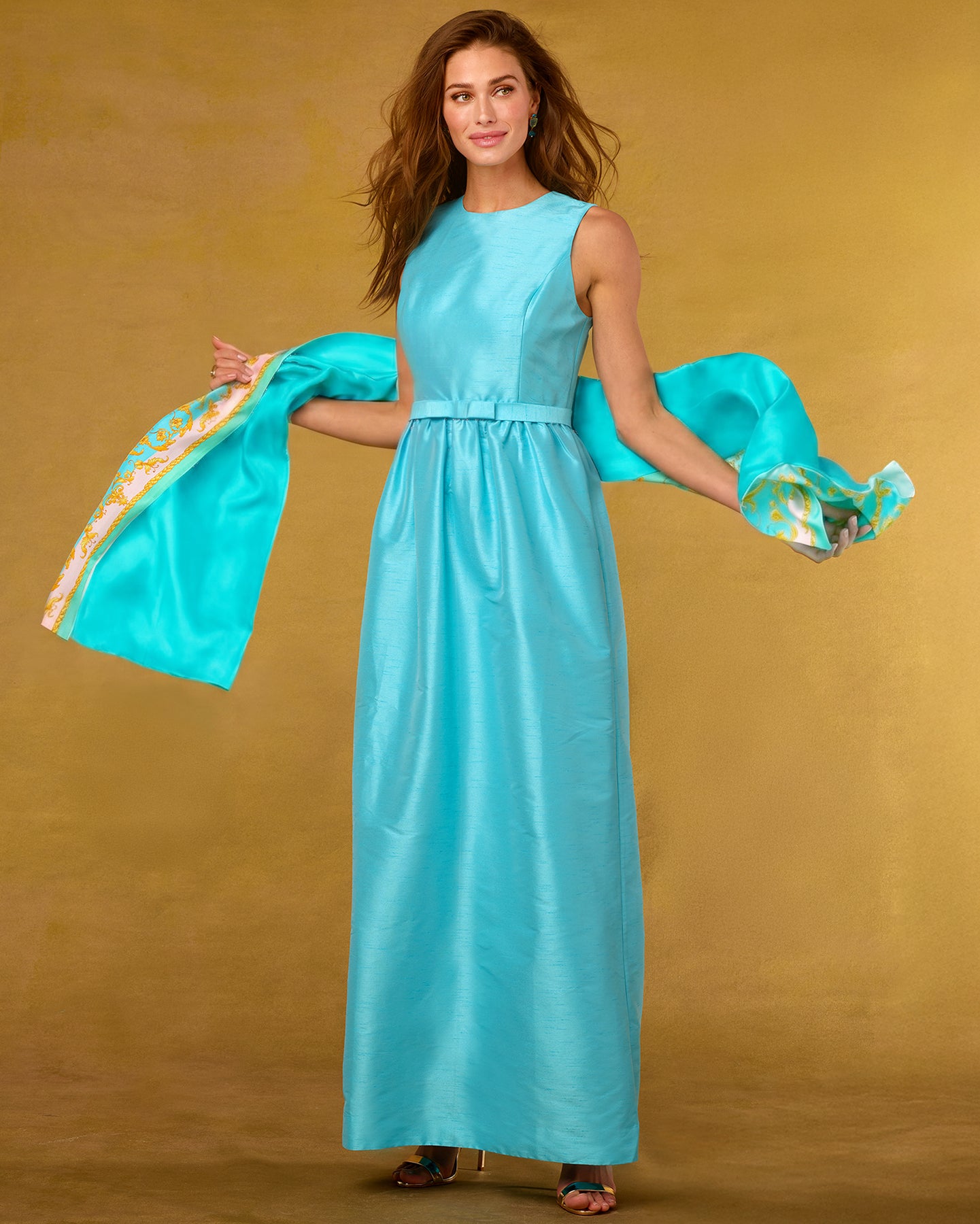 Woman in a turquoise dress holding a matching scarf against a gold background