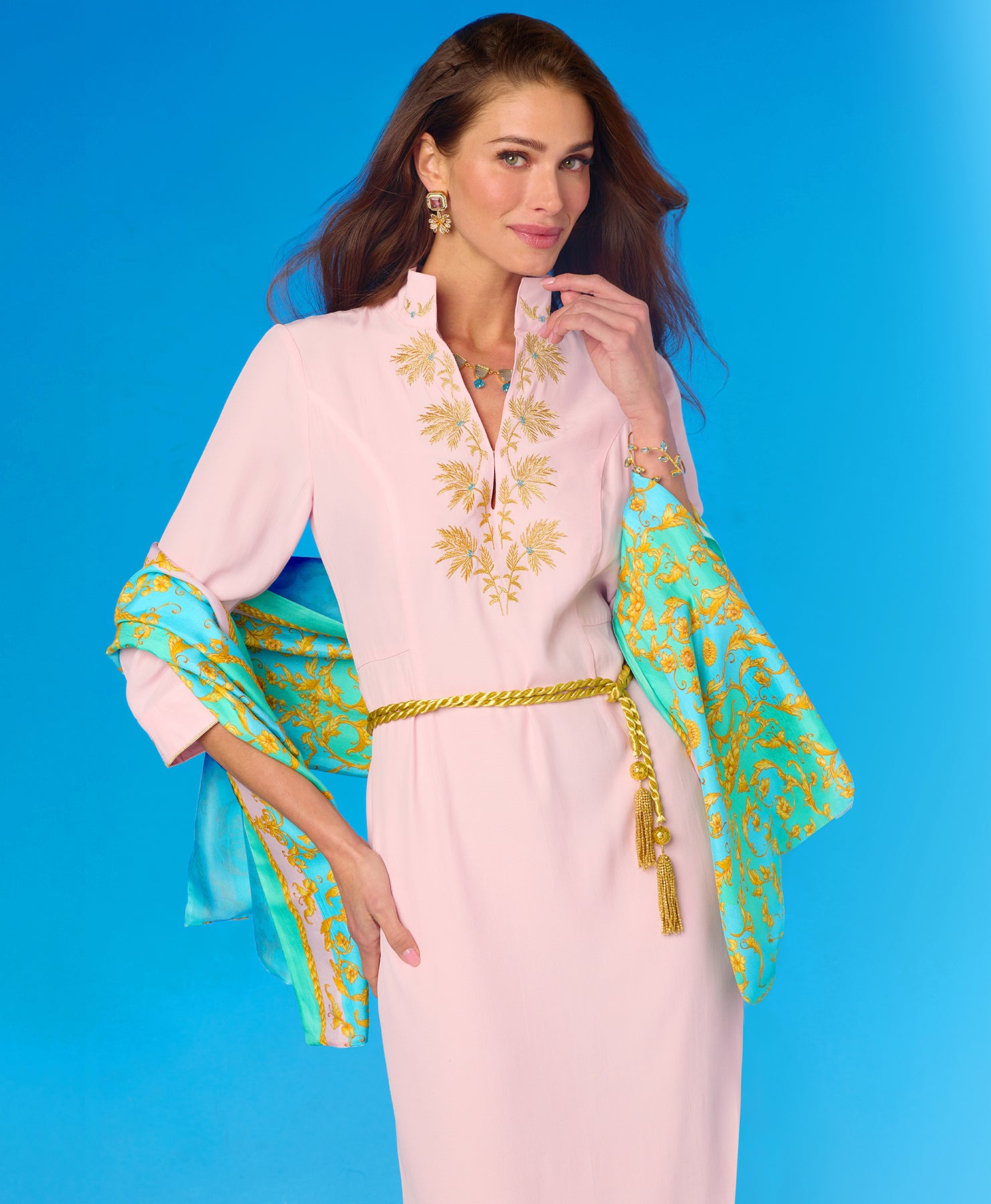 Woman wearing a pink dress with gold and blue embroidery against a blue background