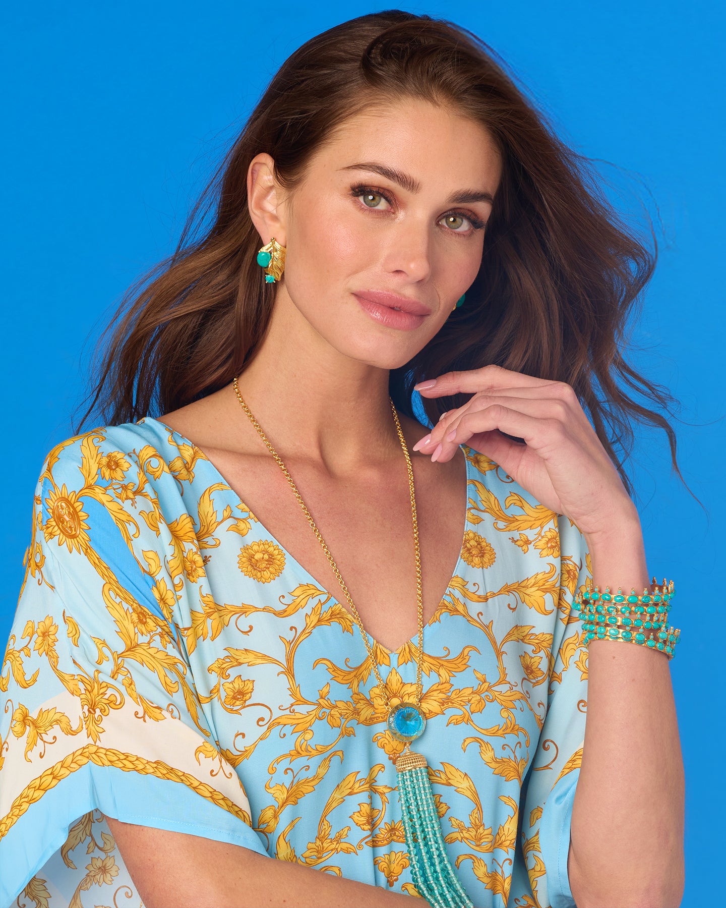 Woman wearing a blue and gold patterned dress with jewelry against a blue background