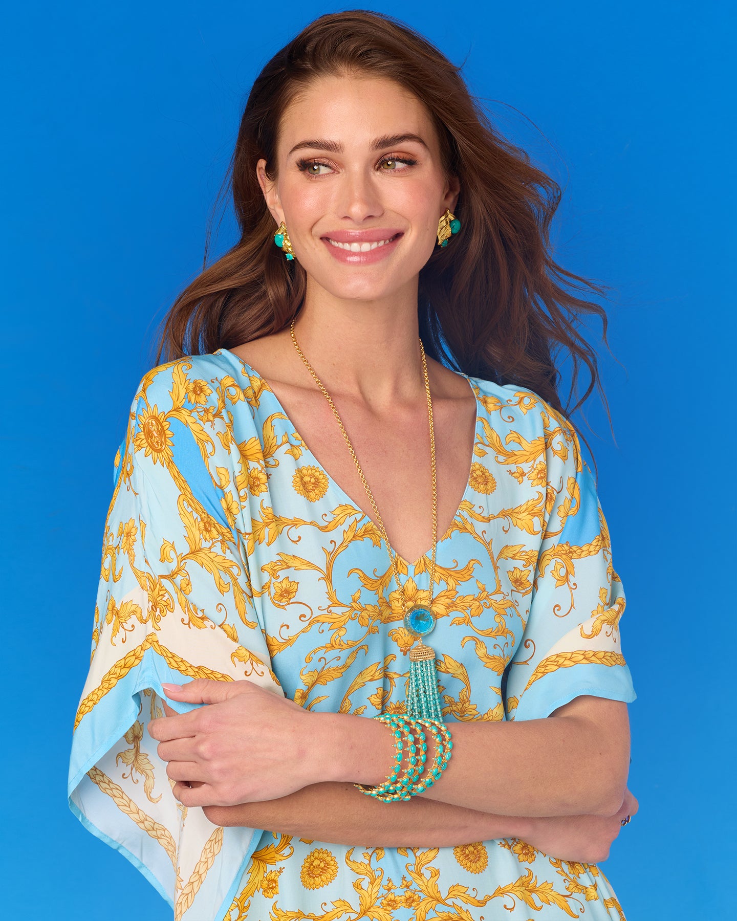 Woman wearing a blue and yellow patterned dress with jewelry against a blue background