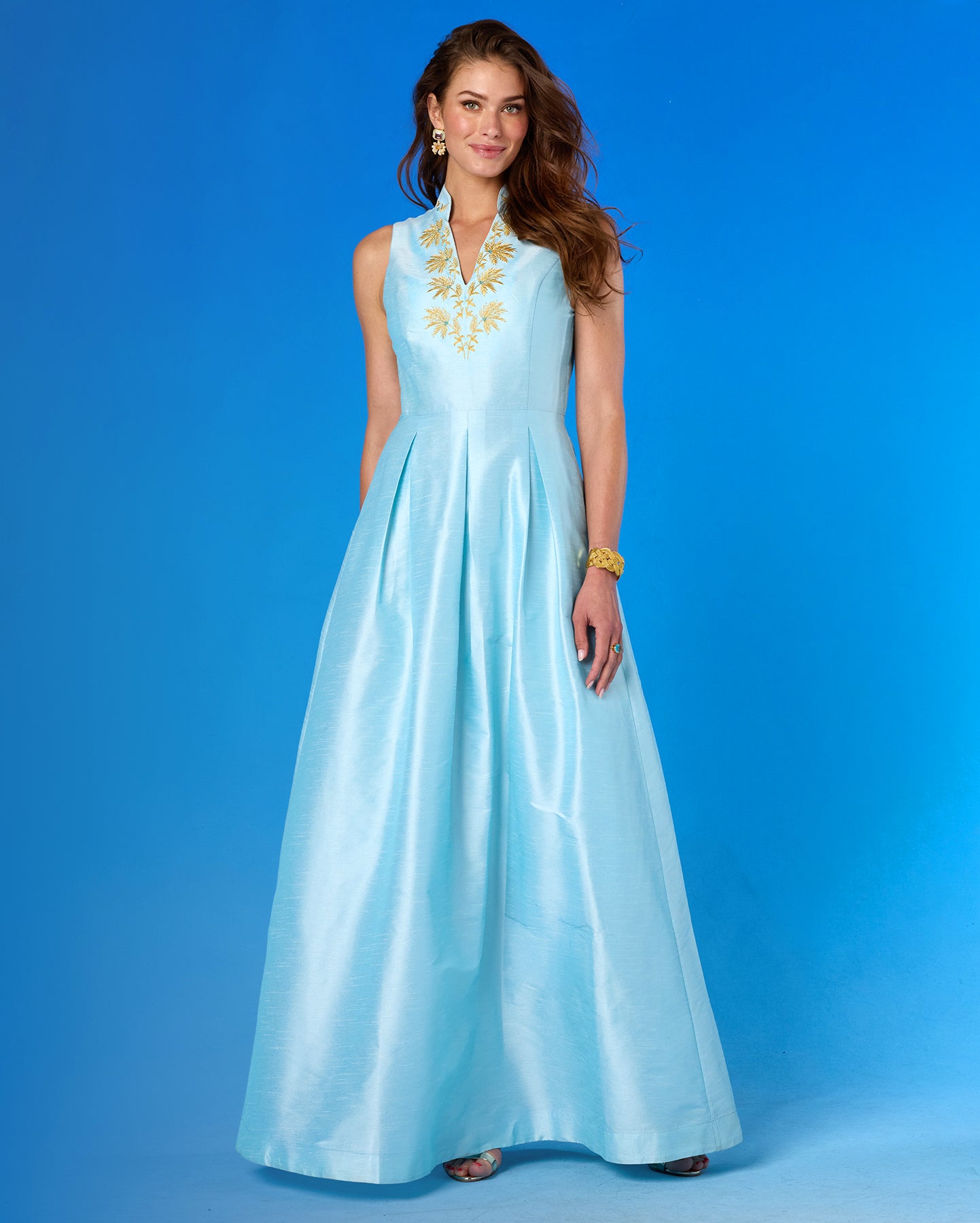 Woman wearing a light blue evening gown with gold embroidery against a blue background