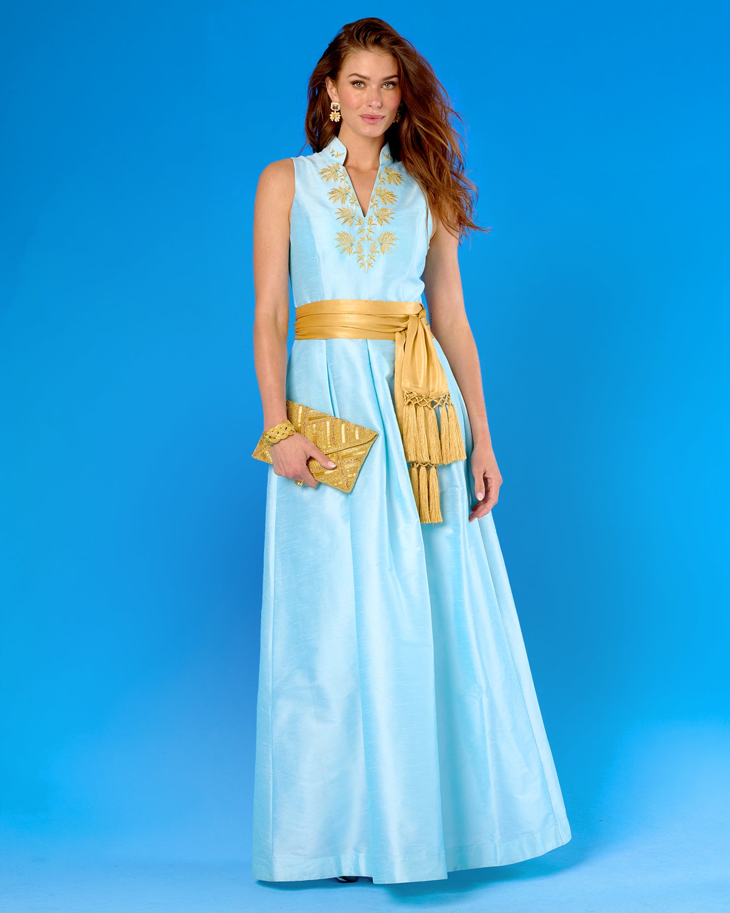 Woman wearing a light blue dress with gold accents against a blue background