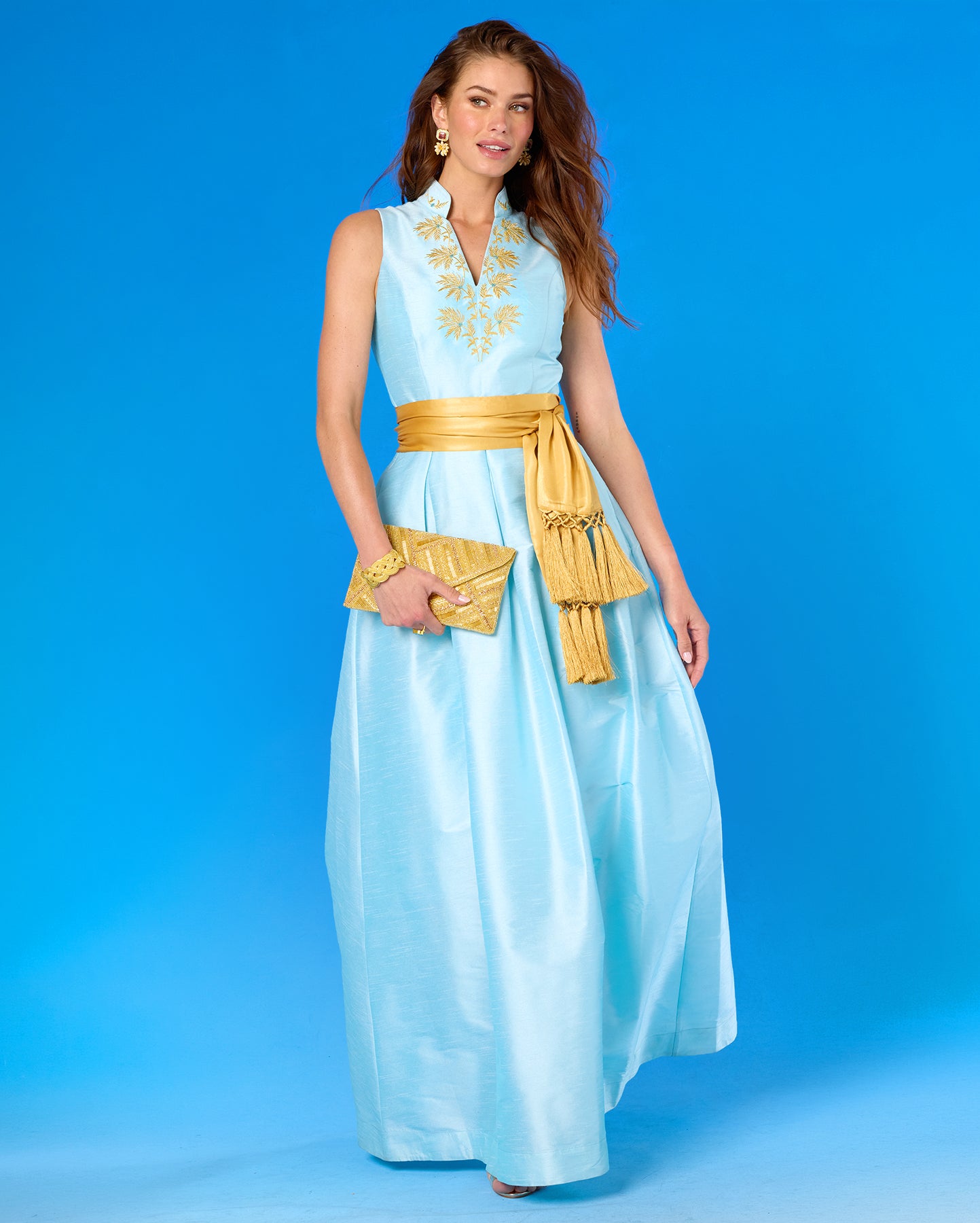 Woman wearing a light blue dress with gold accents against a blue background