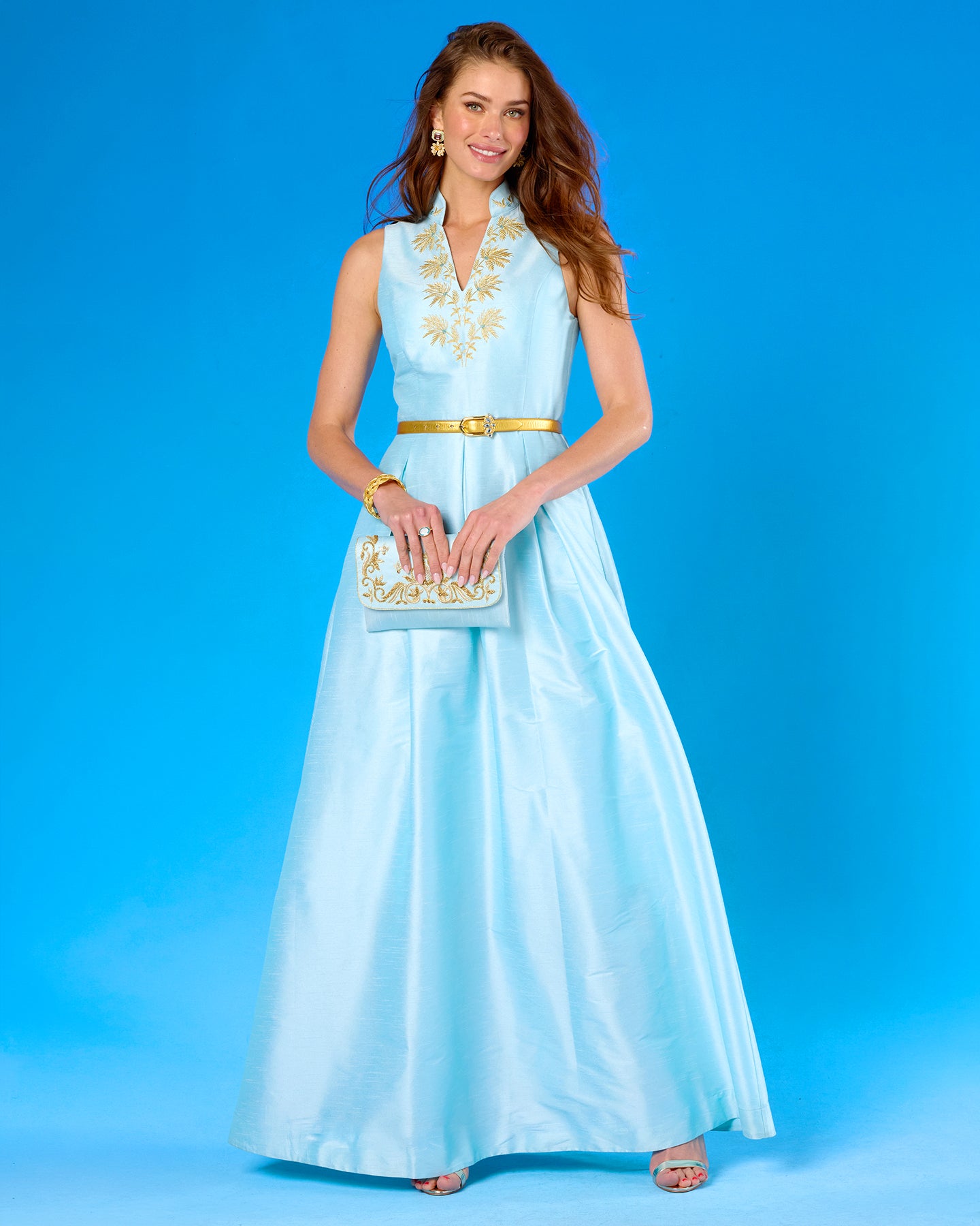 Woman wearing a light blue dress with gold accents against a blue background