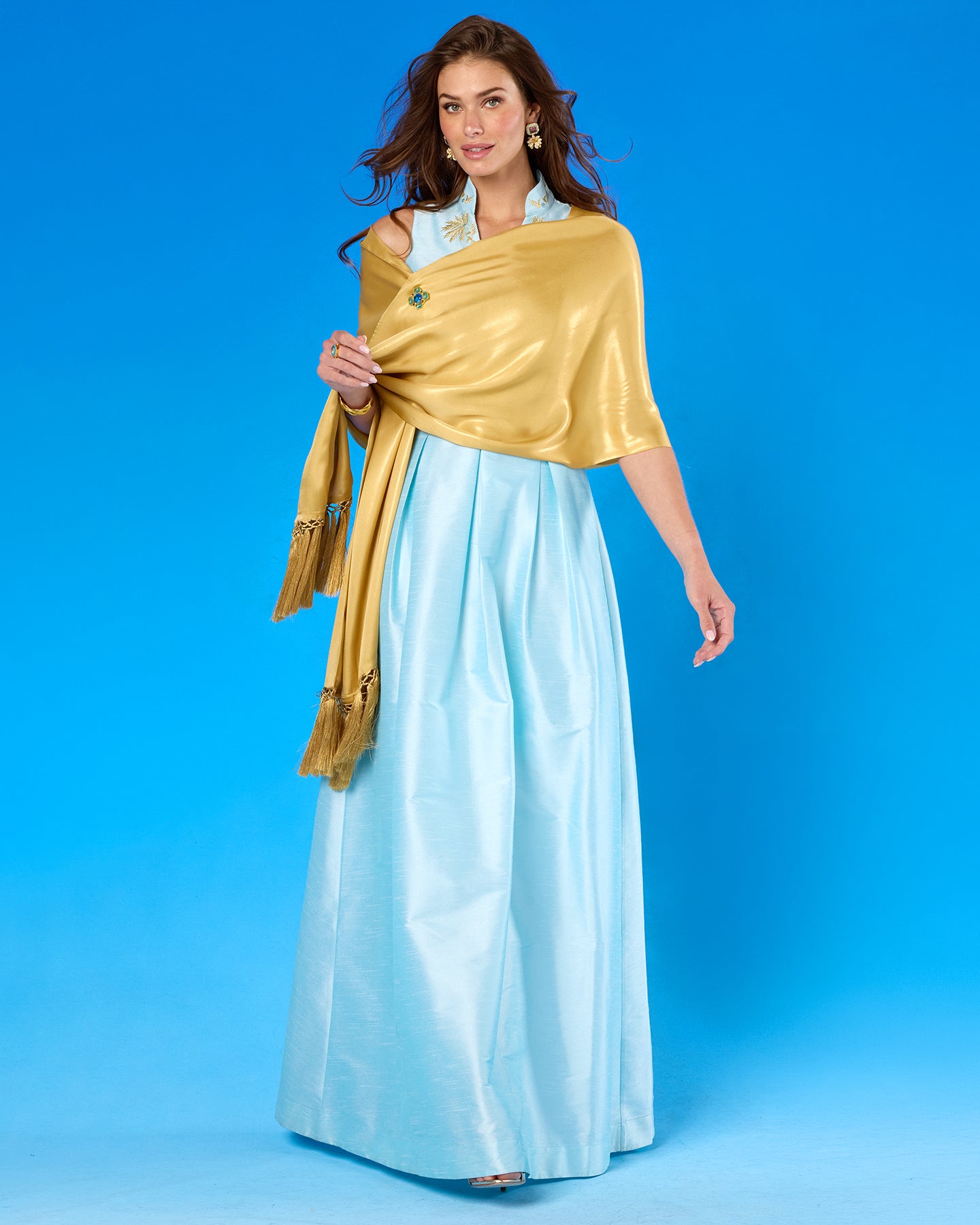 Woman wearing a light blue saree with a gold shawl against a blue background