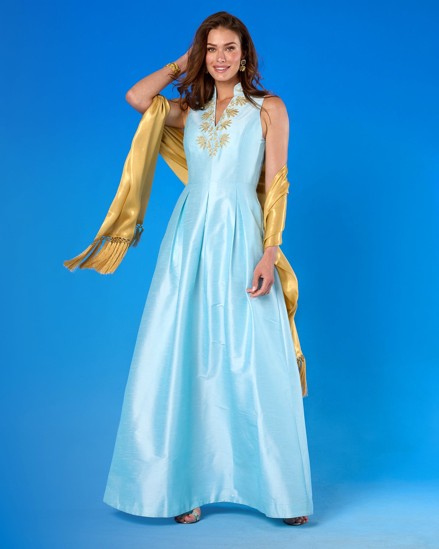 Woman wearing a light blue dress with gold embroidery and a matching shawl against a blue background