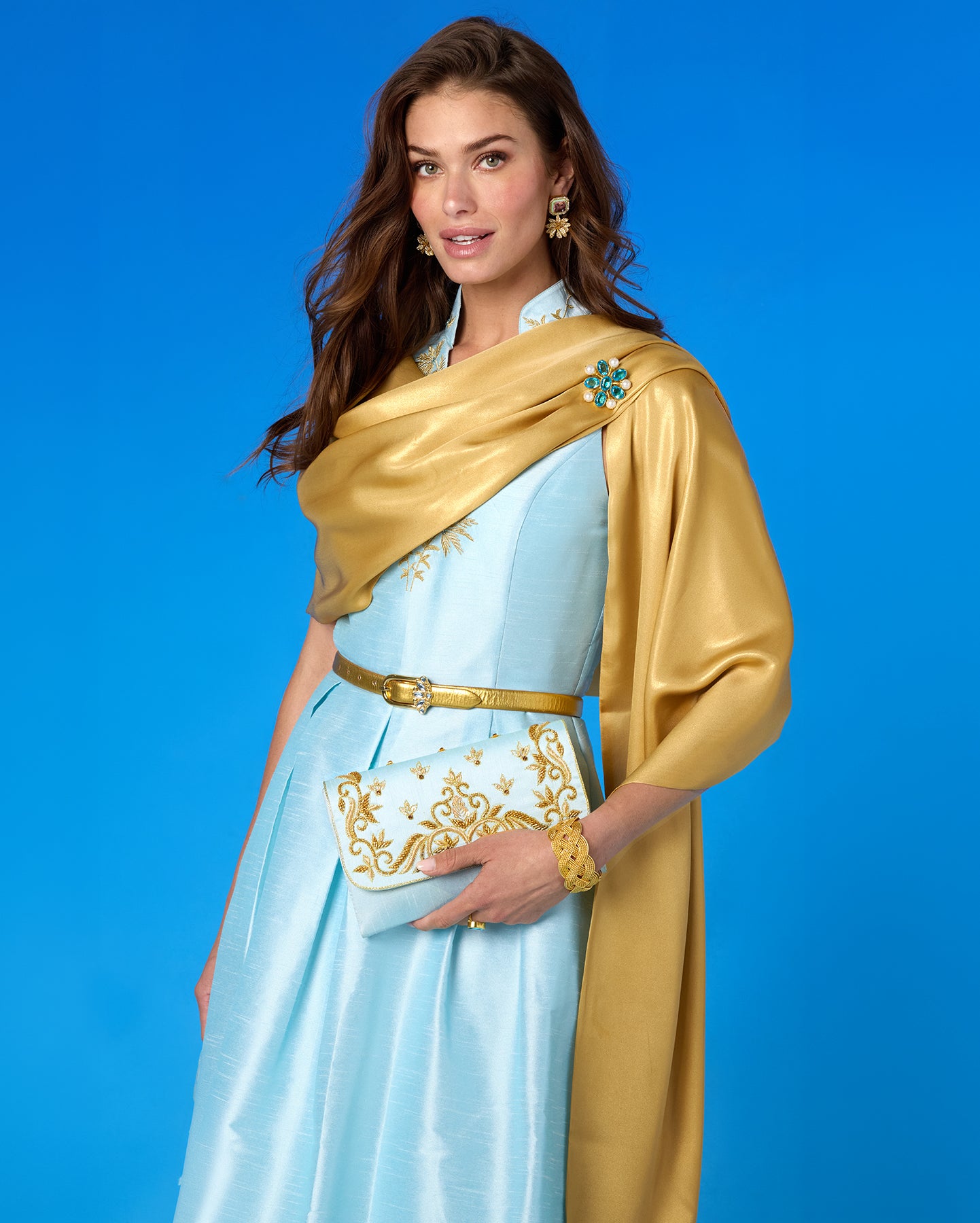Woman wearing a light blue dress with a gold shawl against a blue background