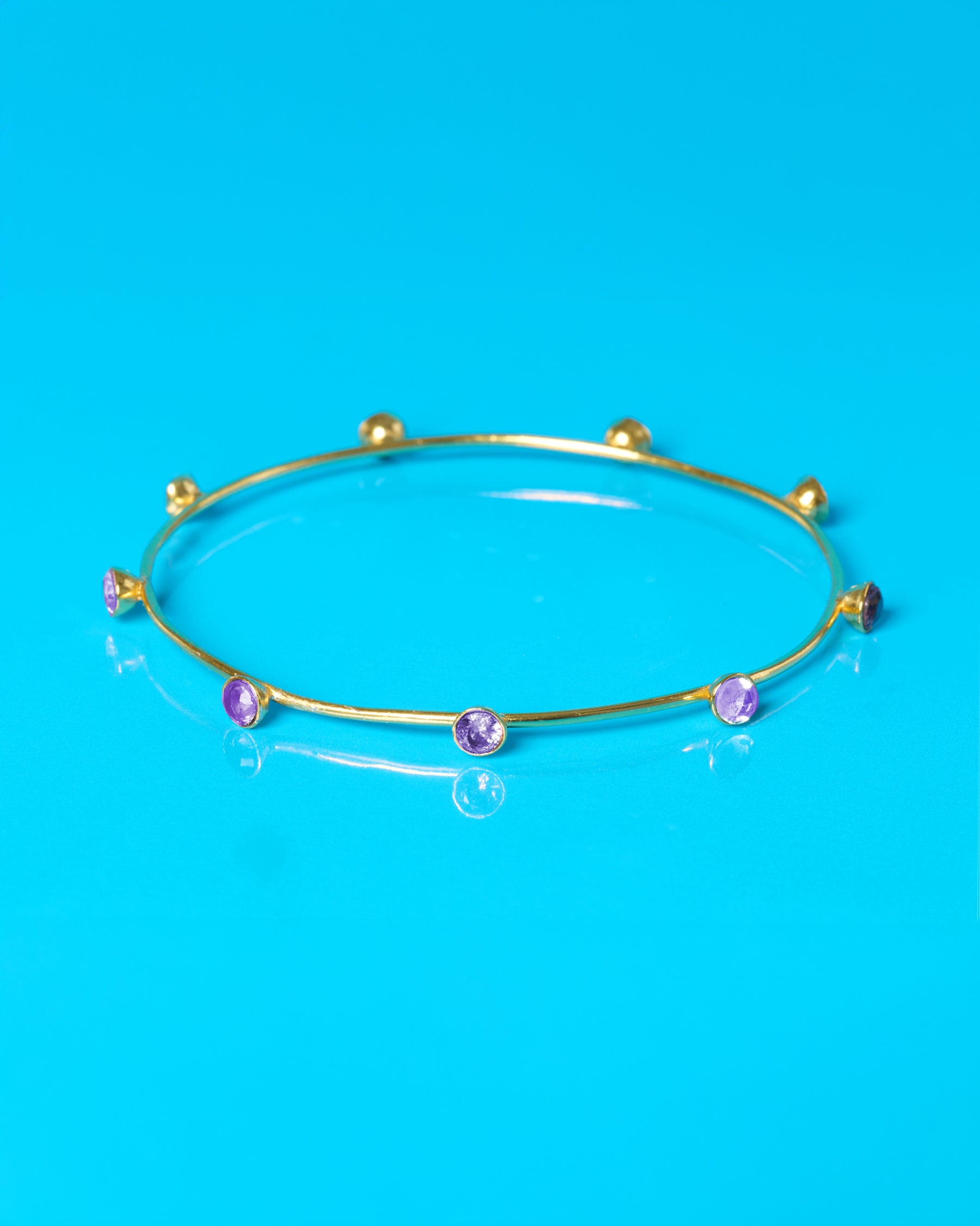 Gold bracelet with purple beads on a blue background