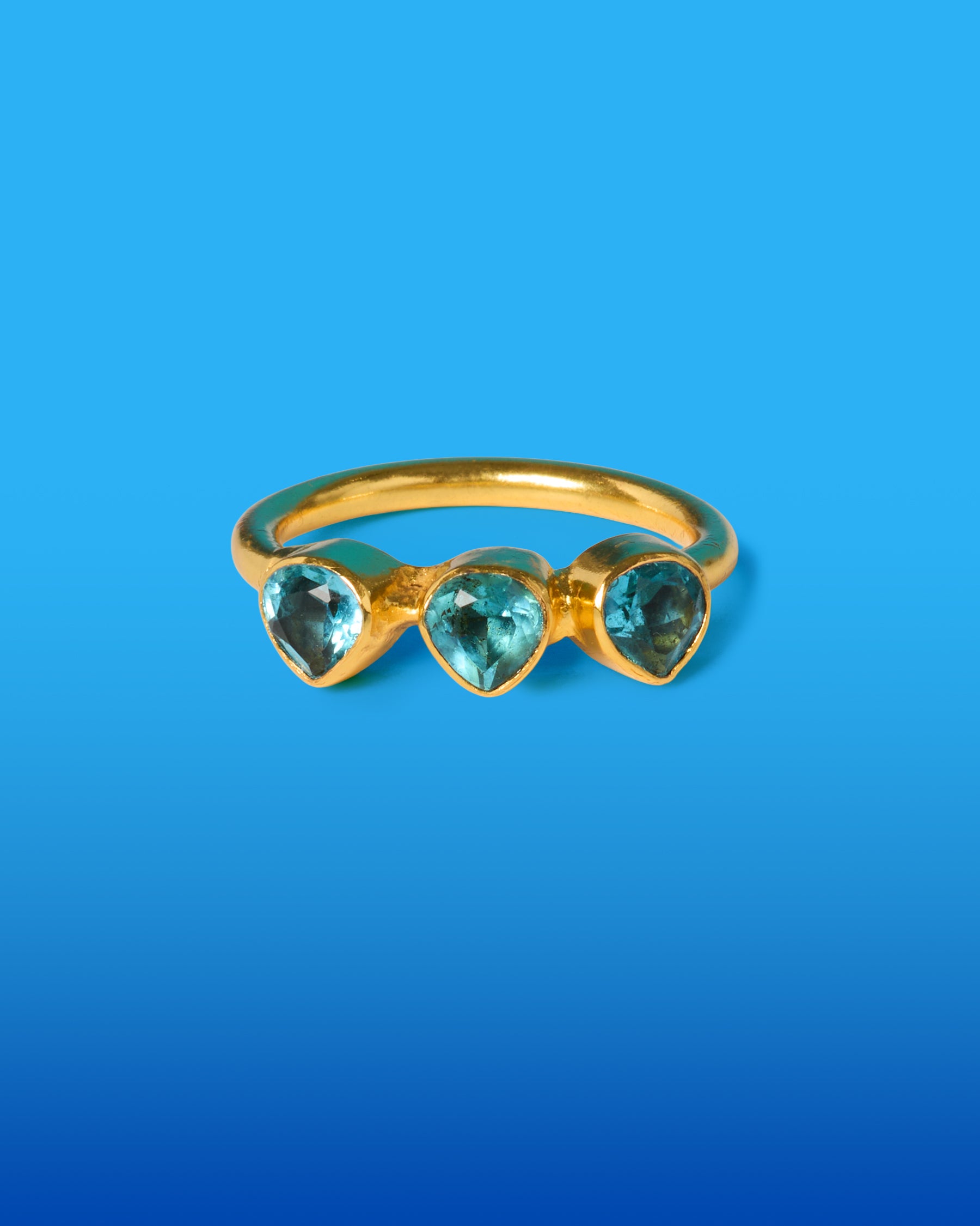 Gold ring with three heart-shaped blue gemstones on a blue background