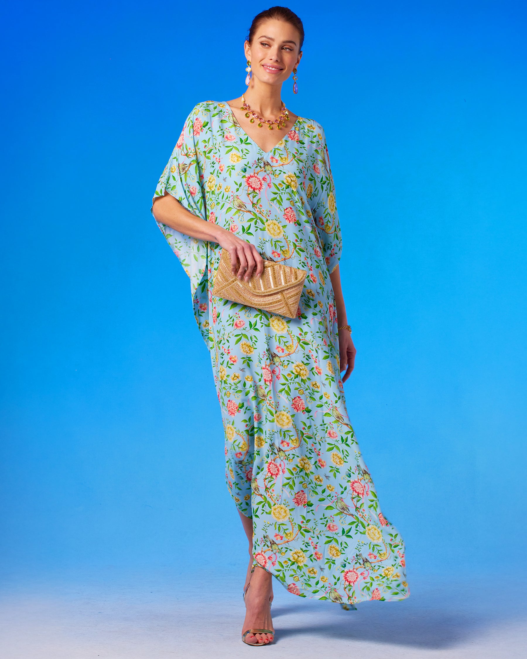 Kallista Kaftan in Antibes Florals front view walking and holding the Betty Gold Beaded Clutch