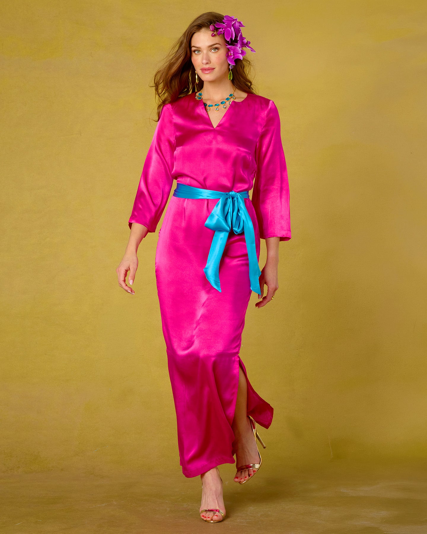 Woman wearing a bright pink dress with a blue belt against a yellow background