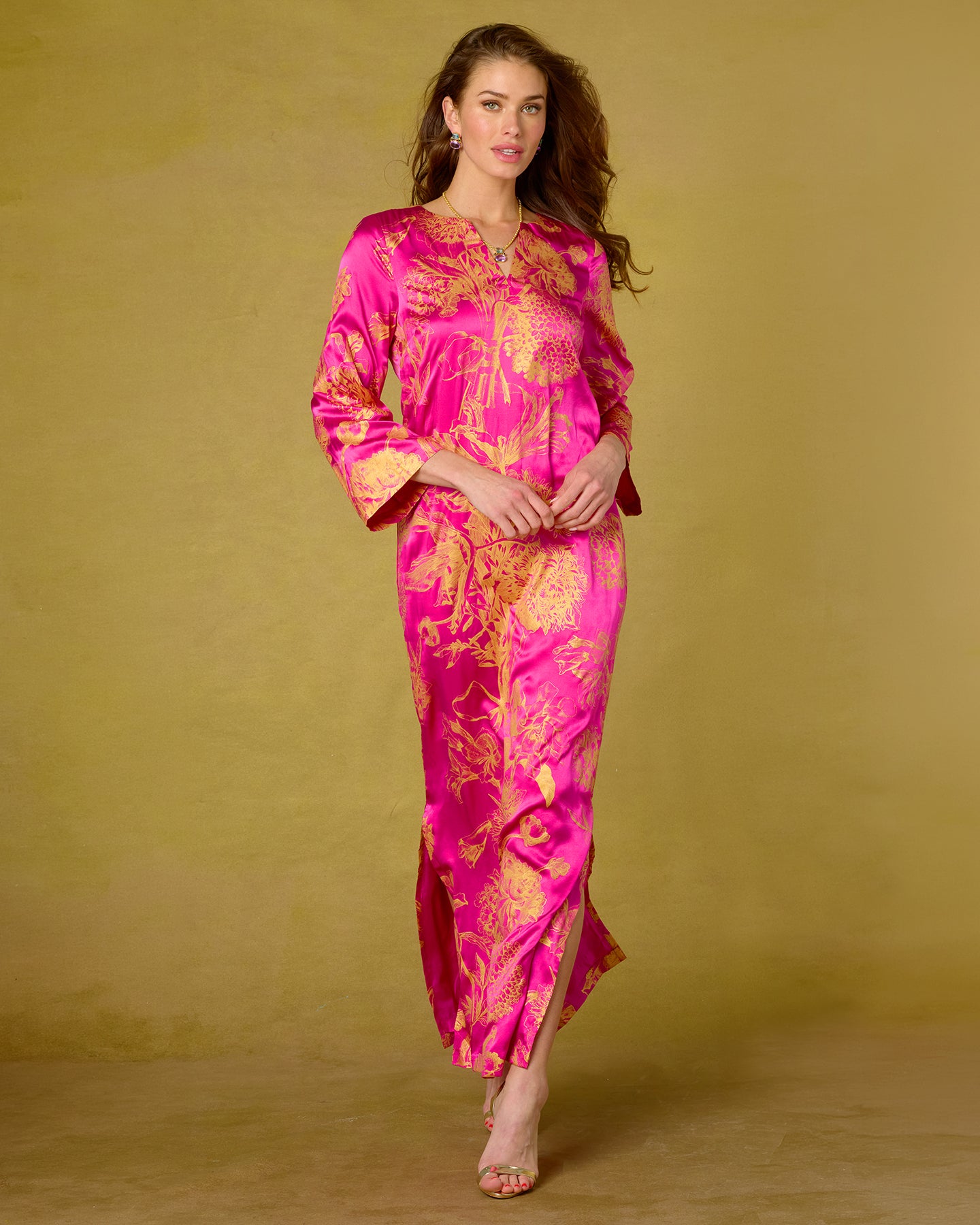 Woman wearing a vibrant pink and gold patterned dress against a plain background