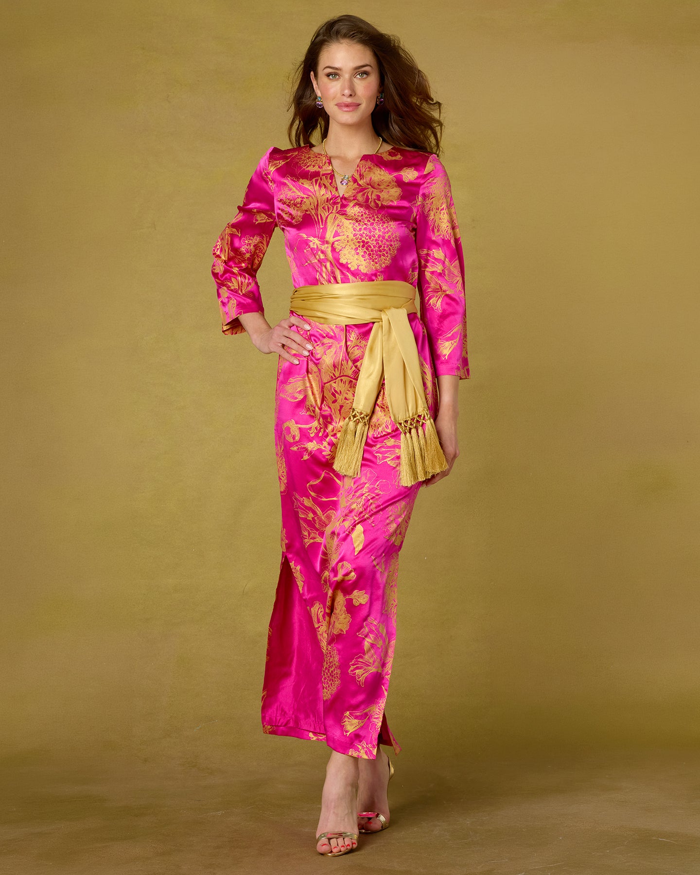 Woman wearing a pink and gold traditional outfit with a belt on a beige background