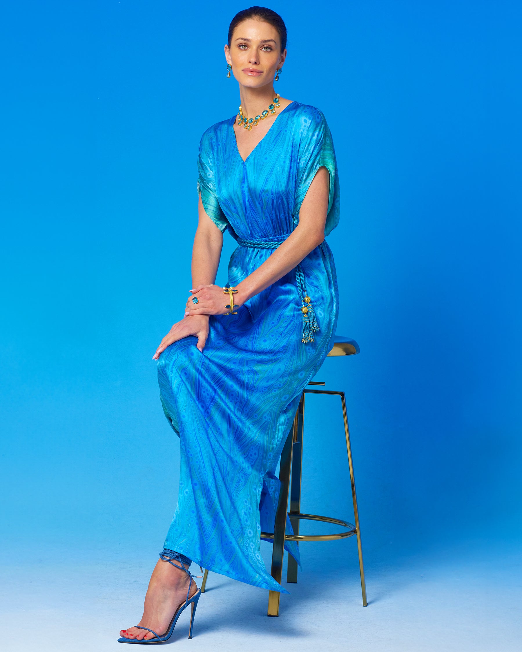 Calliope Long Silk Dress in Sea Nymph Blues witting on a gold chair