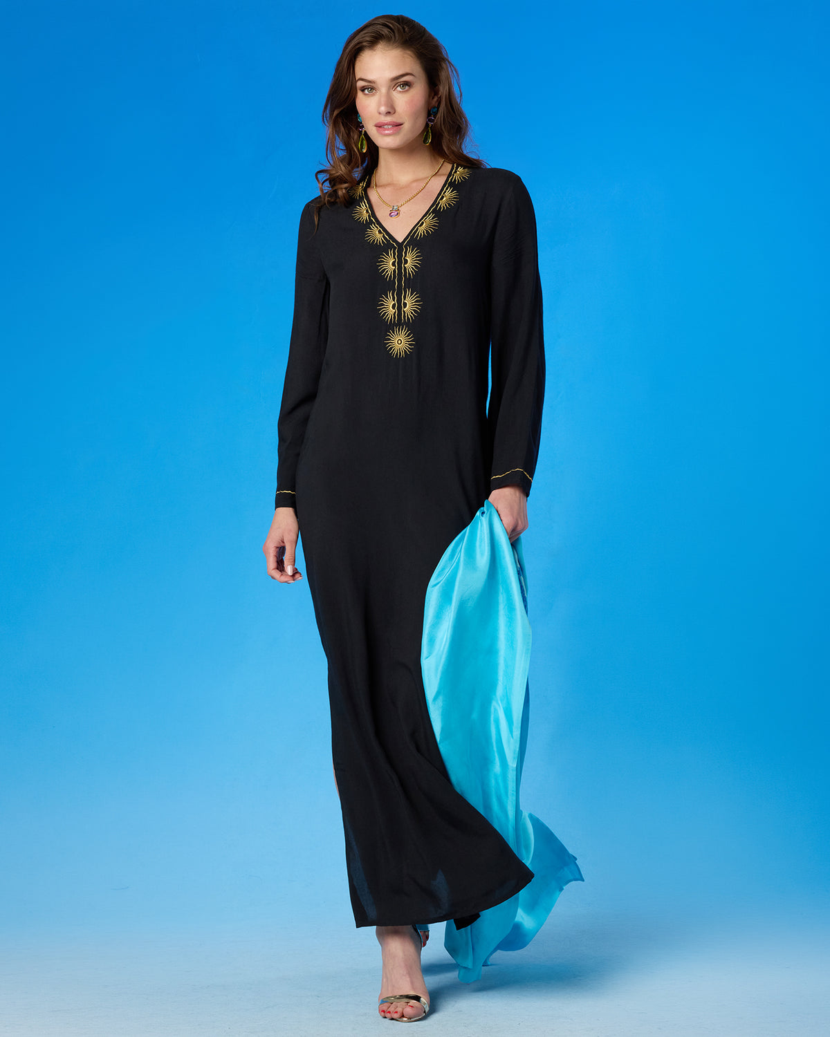 Woman wearing a black dress with gold embroidery holding a blue scarf against a blue background