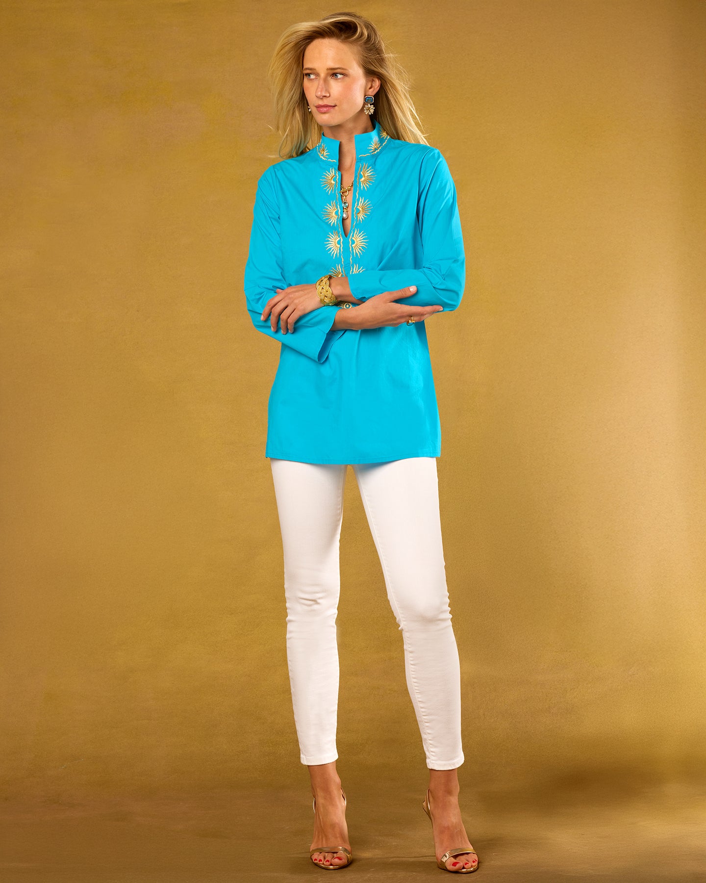 Woman wearing a blue embroidered top and white pants against a beige background