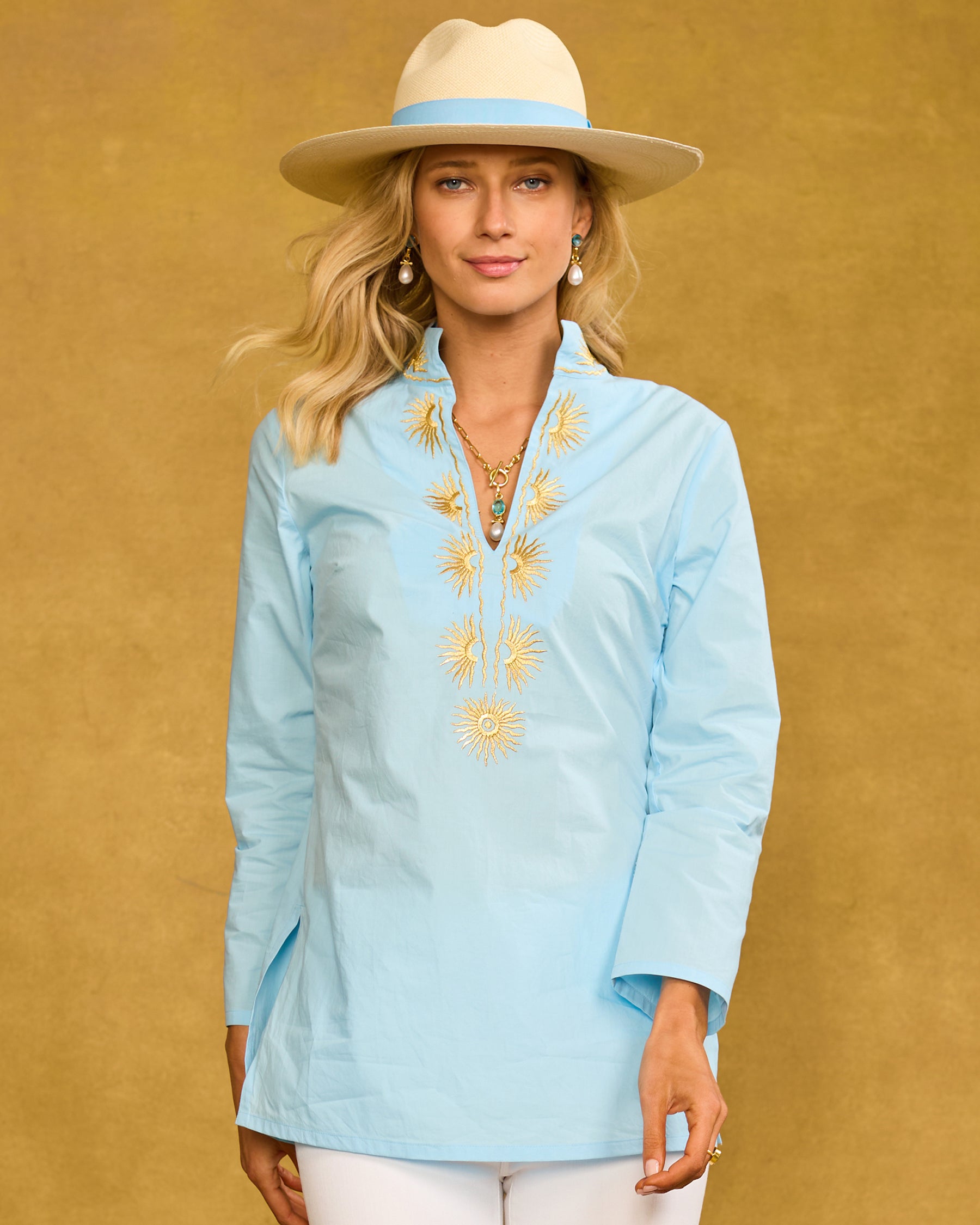 Woman wearing a light blue embroidered blouse and beige hat against a yellow background