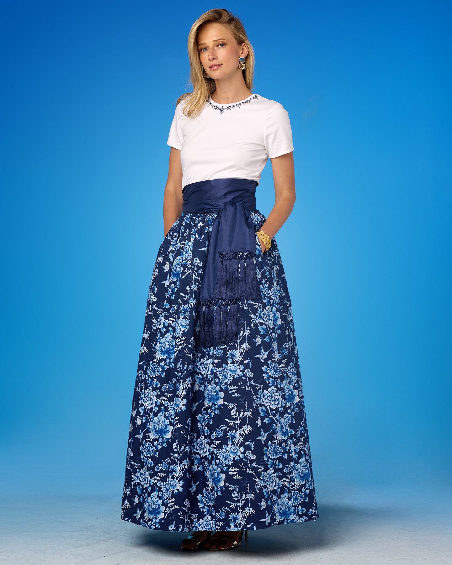 Woman wearing a white top and blue floral skirt against a blue background