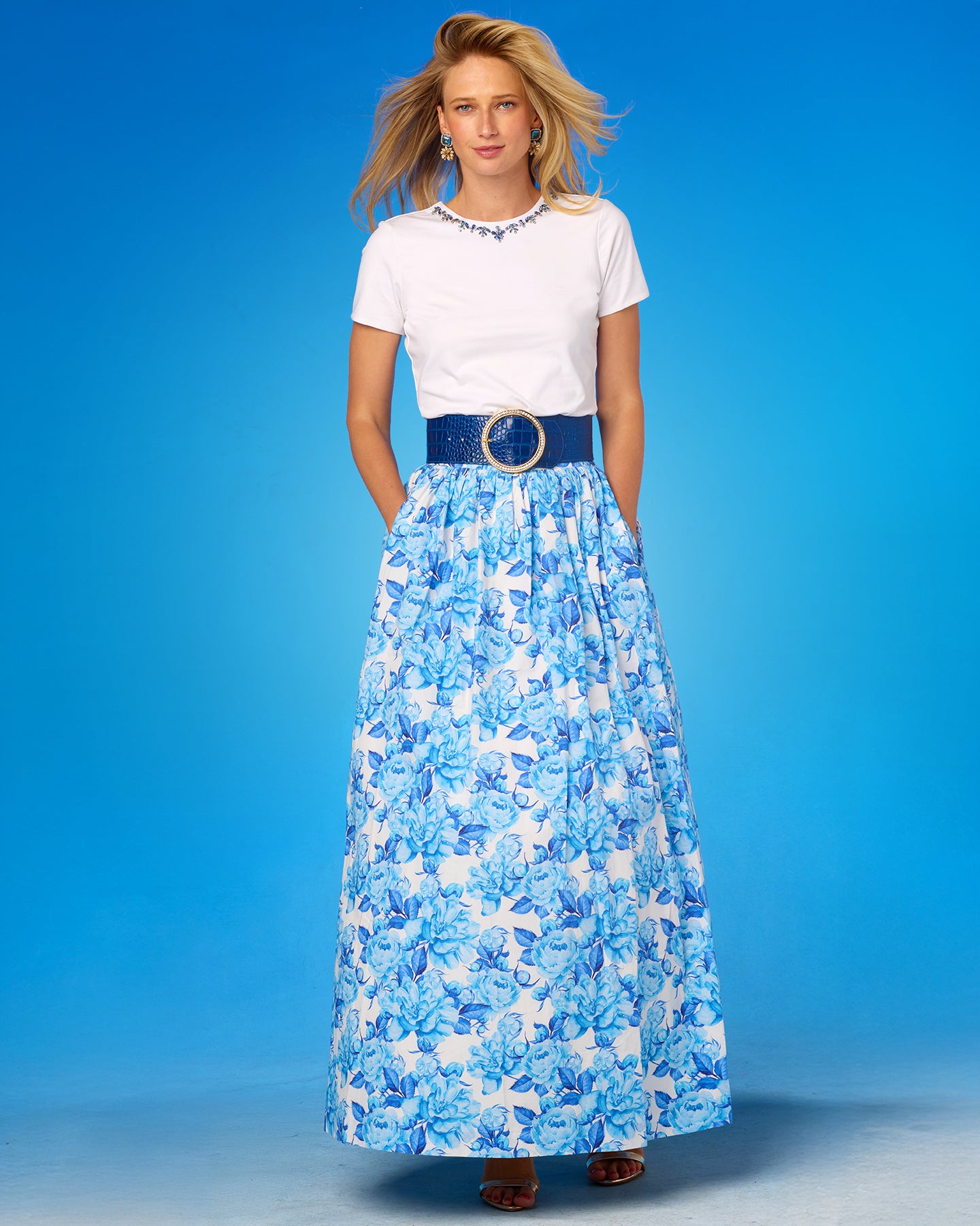 Woman wearing a white top and blue floral skirt against a blue background