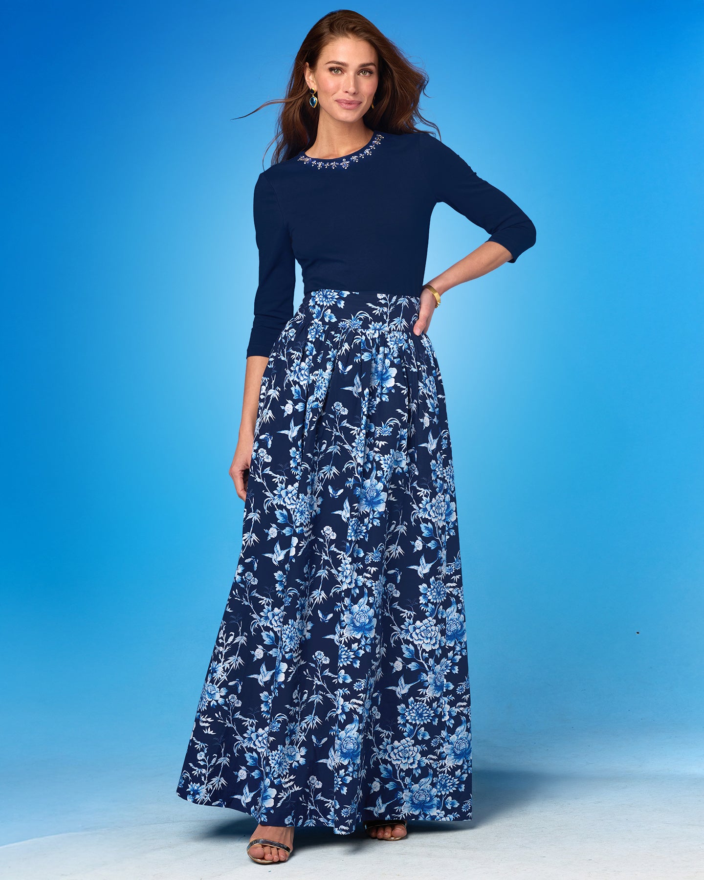Woman wearing a navy top and blue floral skirt against a blue background