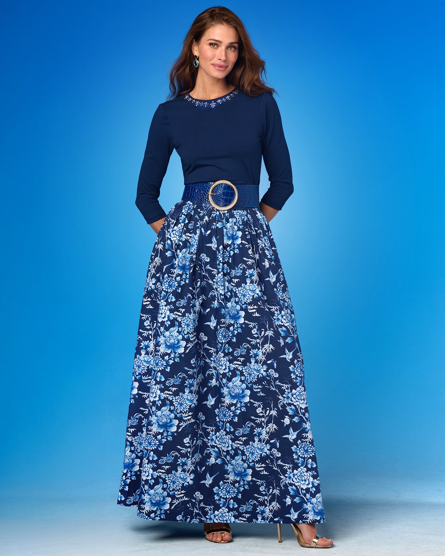 Woman wearing a navy top and blue floral skirt against a blue background