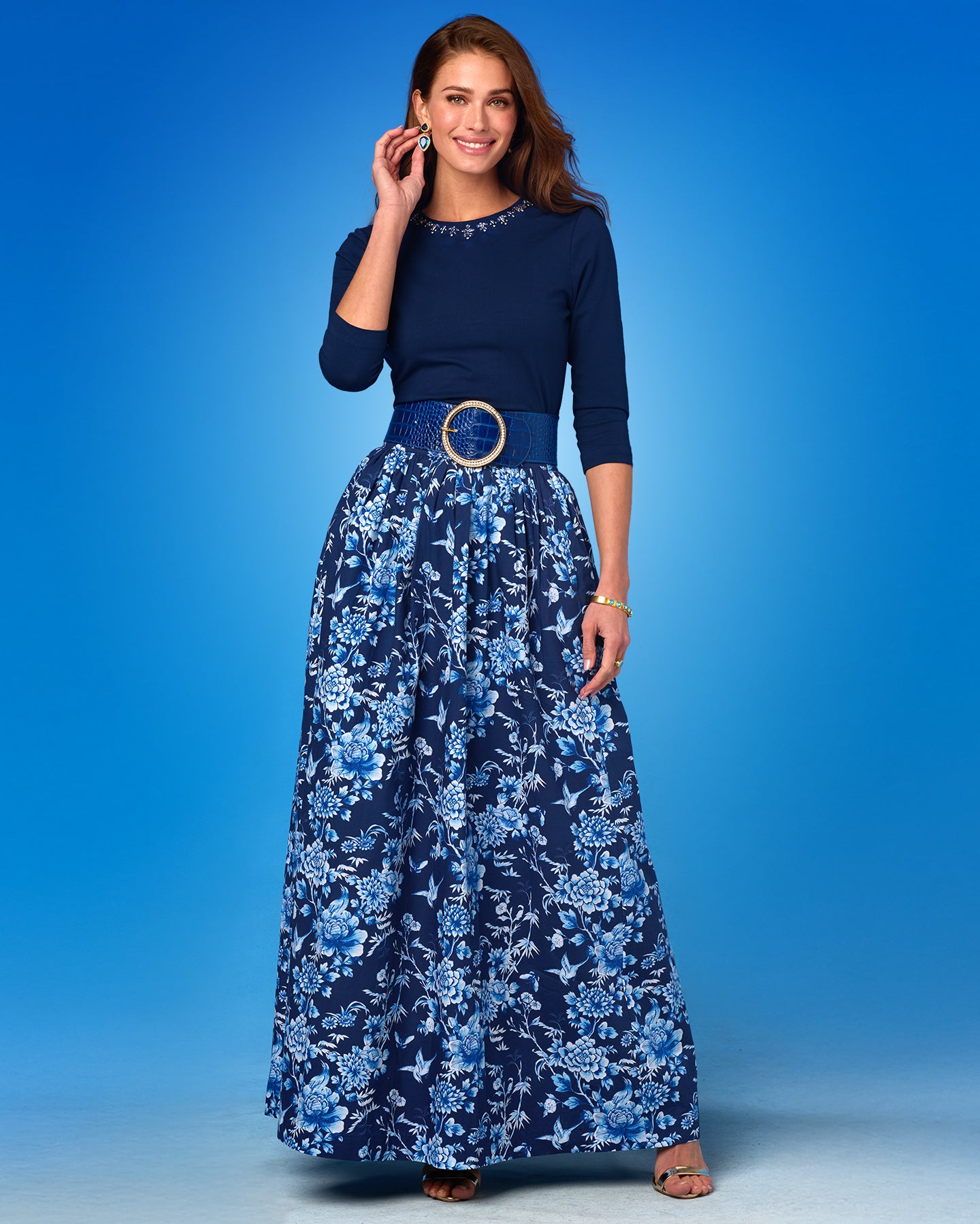 Woman wearing a navy blue top and floral skirt against a blue background