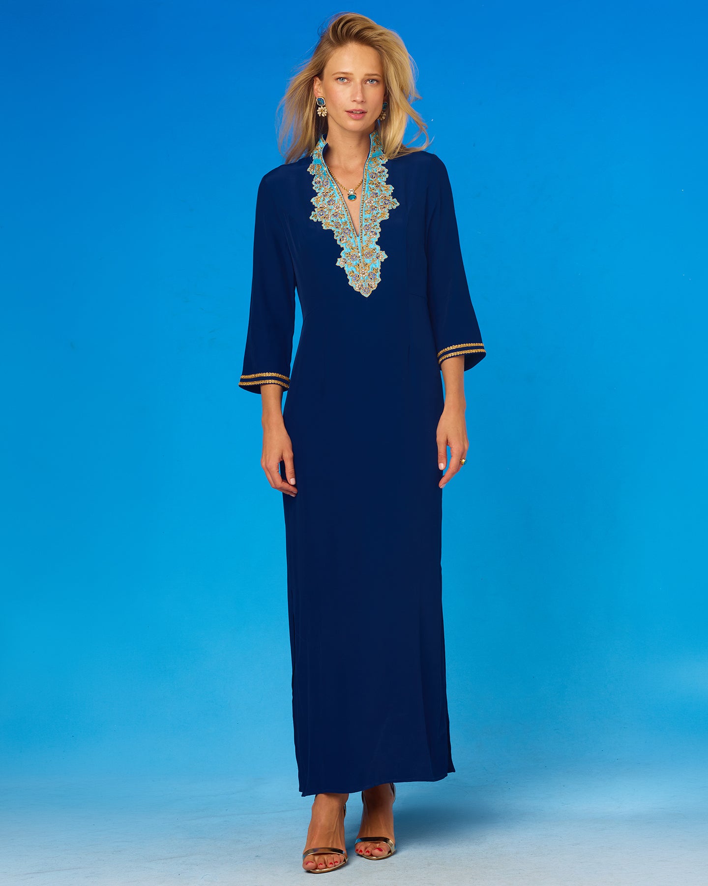 Woman wearing a long blue dress with intricate detailing on a blue background