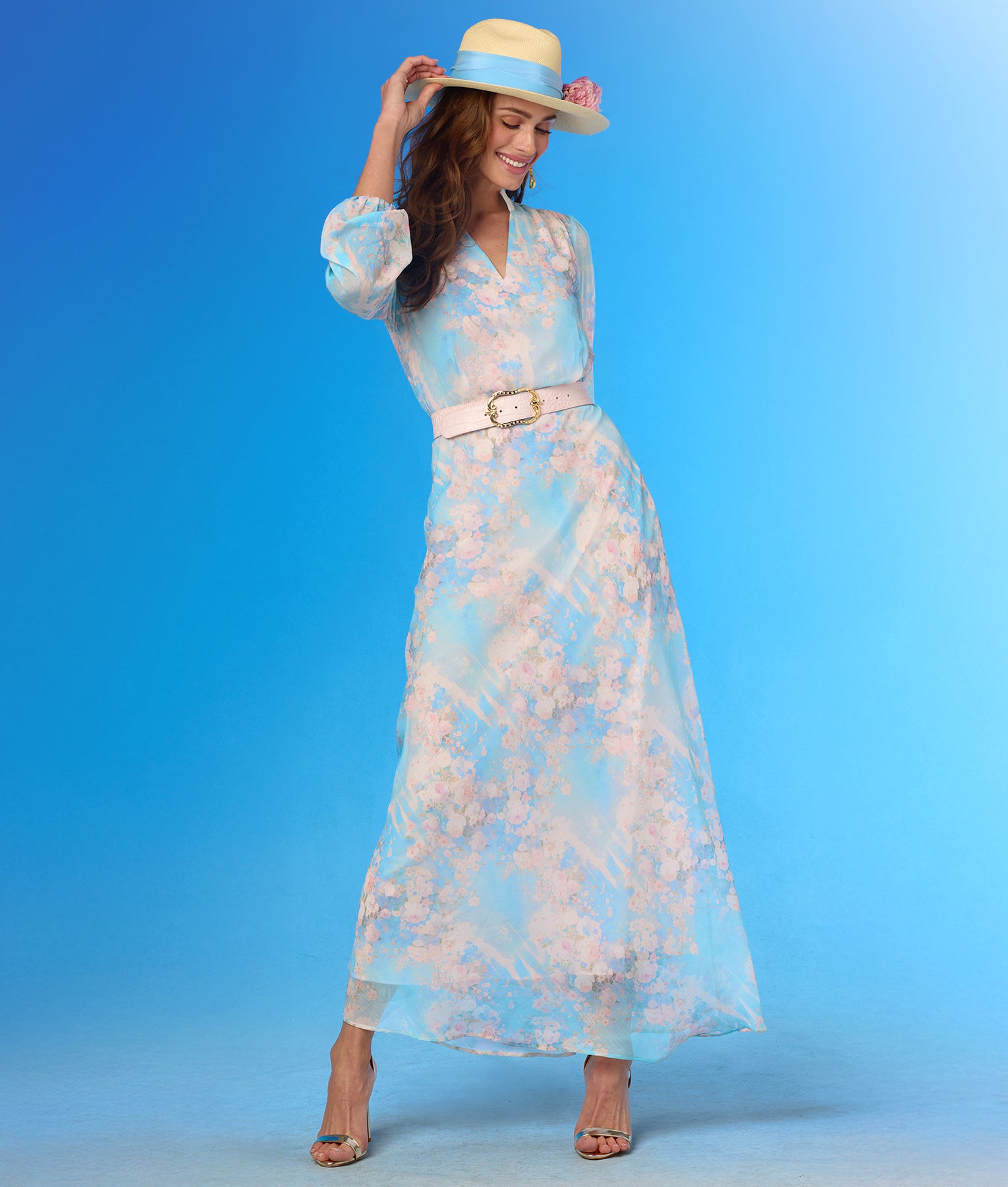 Woman wearing a floral dress and hat against a blue background looking down
