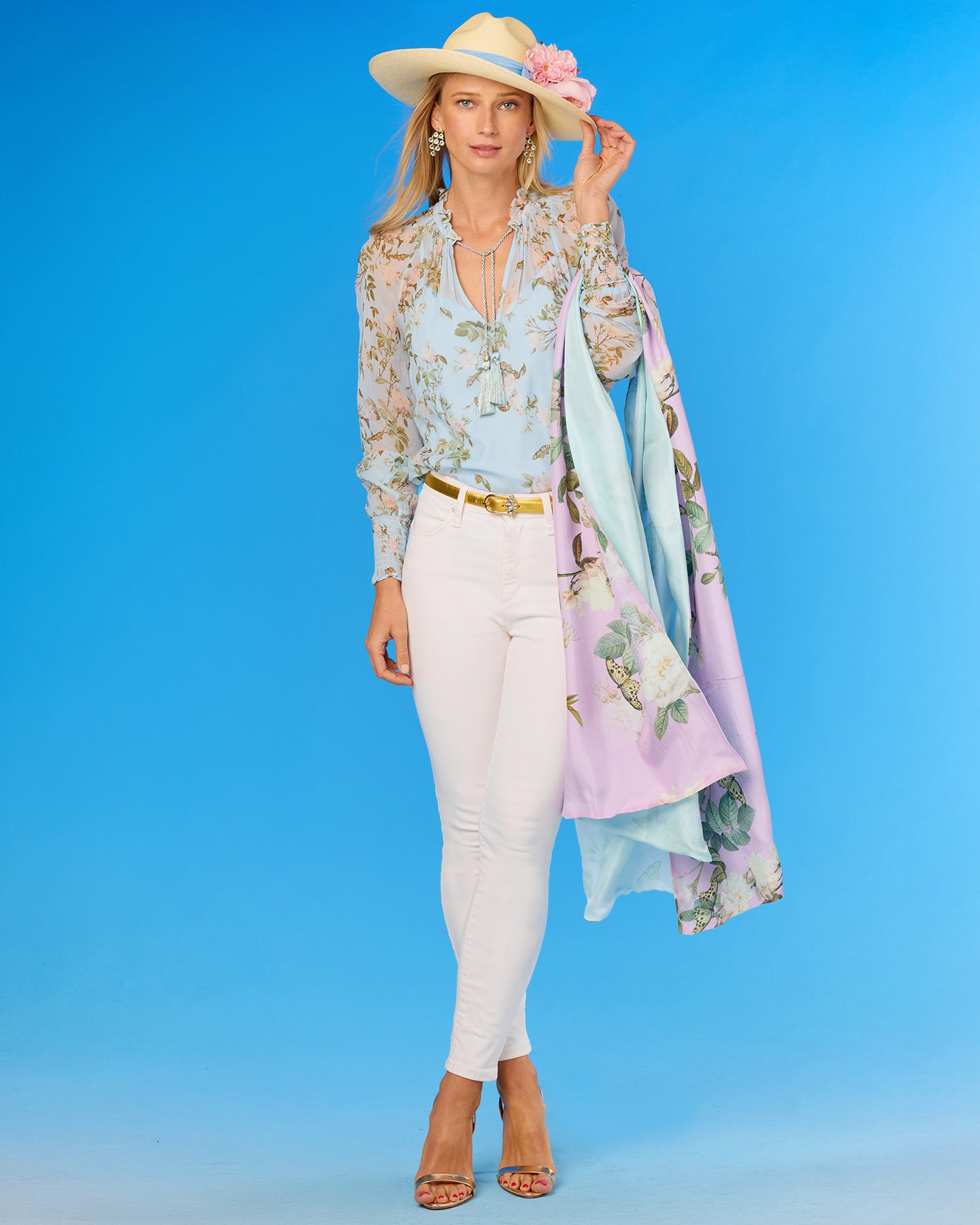 Woman wearing a floral outfit with a hat and scarf against a blue background