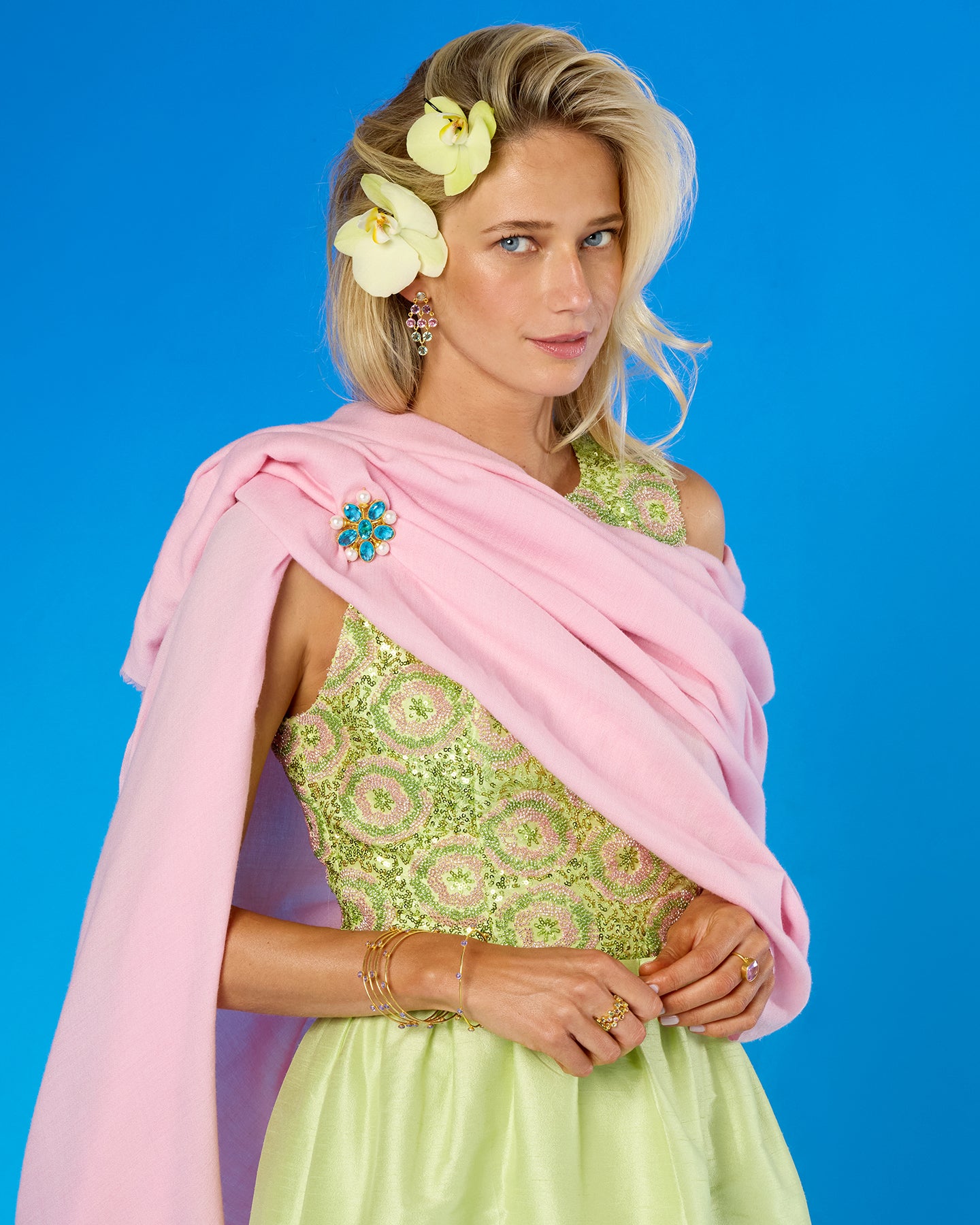 A woman models a light pink dupatta draped over her shoulders, paired with a light green embroidered dress, set against a solid blue studio background.