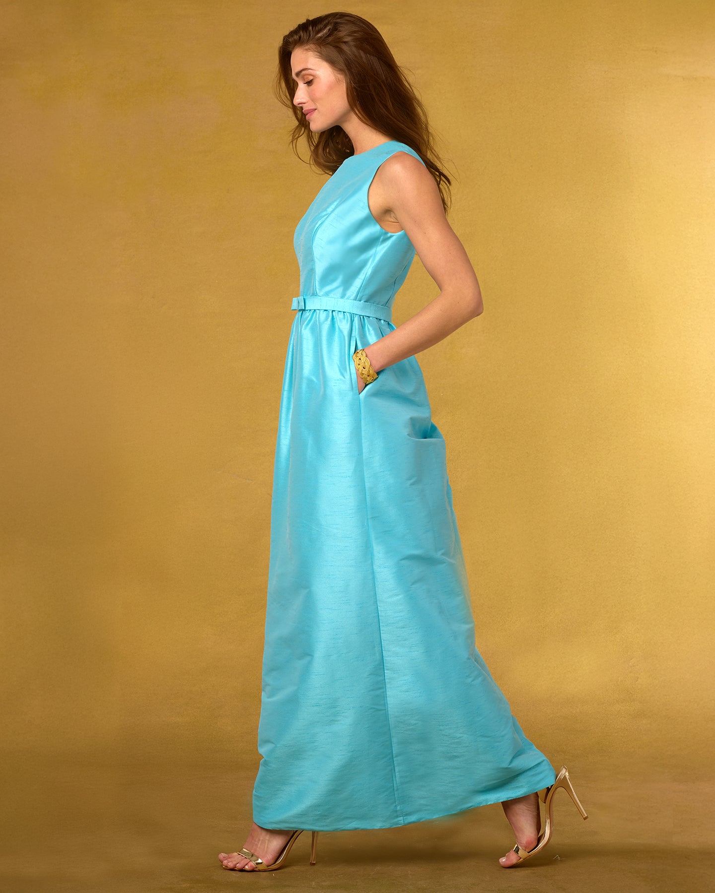 Side view of a woman wearing a blue dress against a gold background