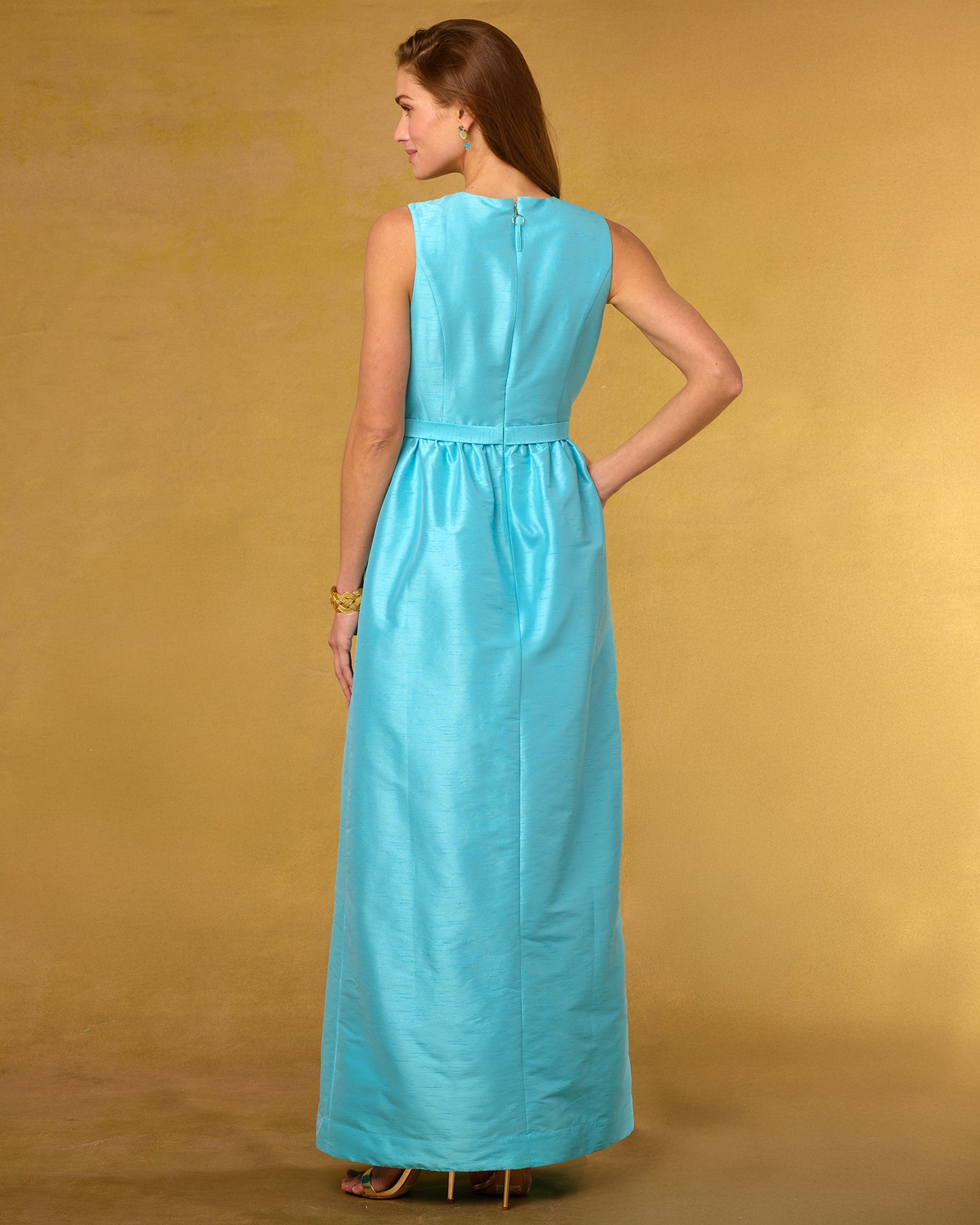 Back view of a woman wearing a turquoise dress against a beige background