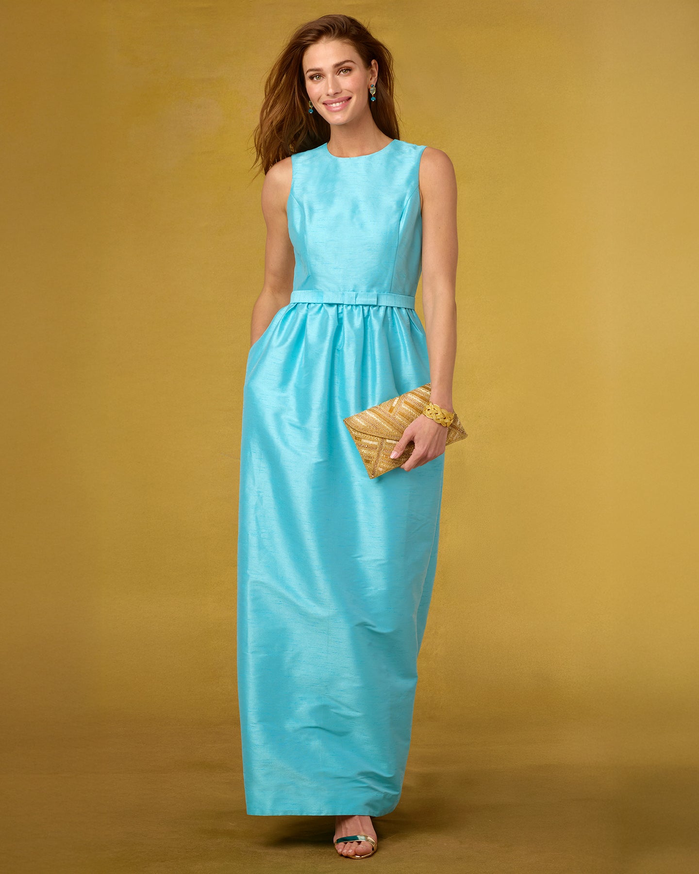 Woman in a turquoise dress holding a gold clutch against a yellow background