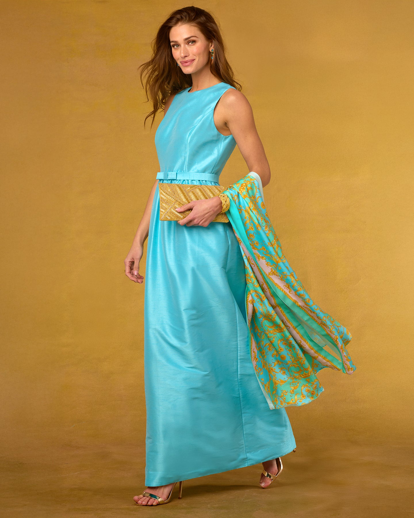 Woman in a turquoise dress holding a matching shawl against a mustard yellow background