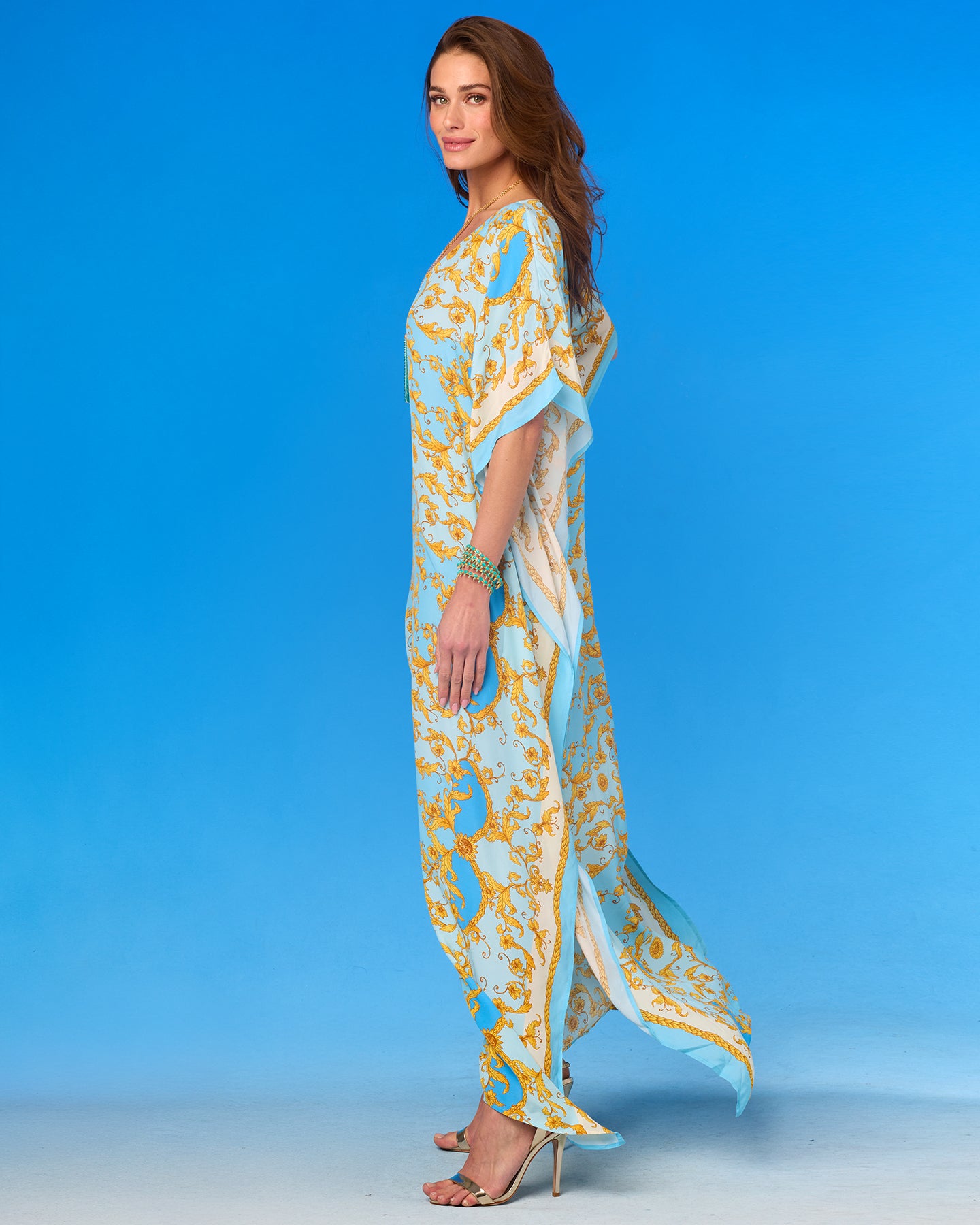 Woman wearing a long, light blue and gold patterned dress against a clear blue background