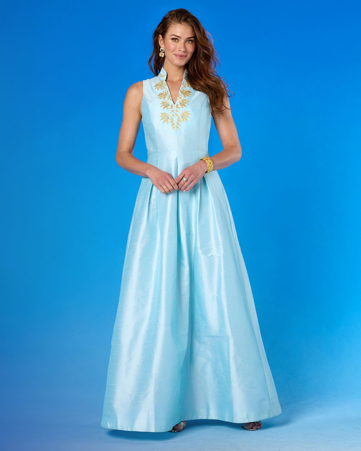 Woman wearing a light blue dress with gold embroidery on a blue background