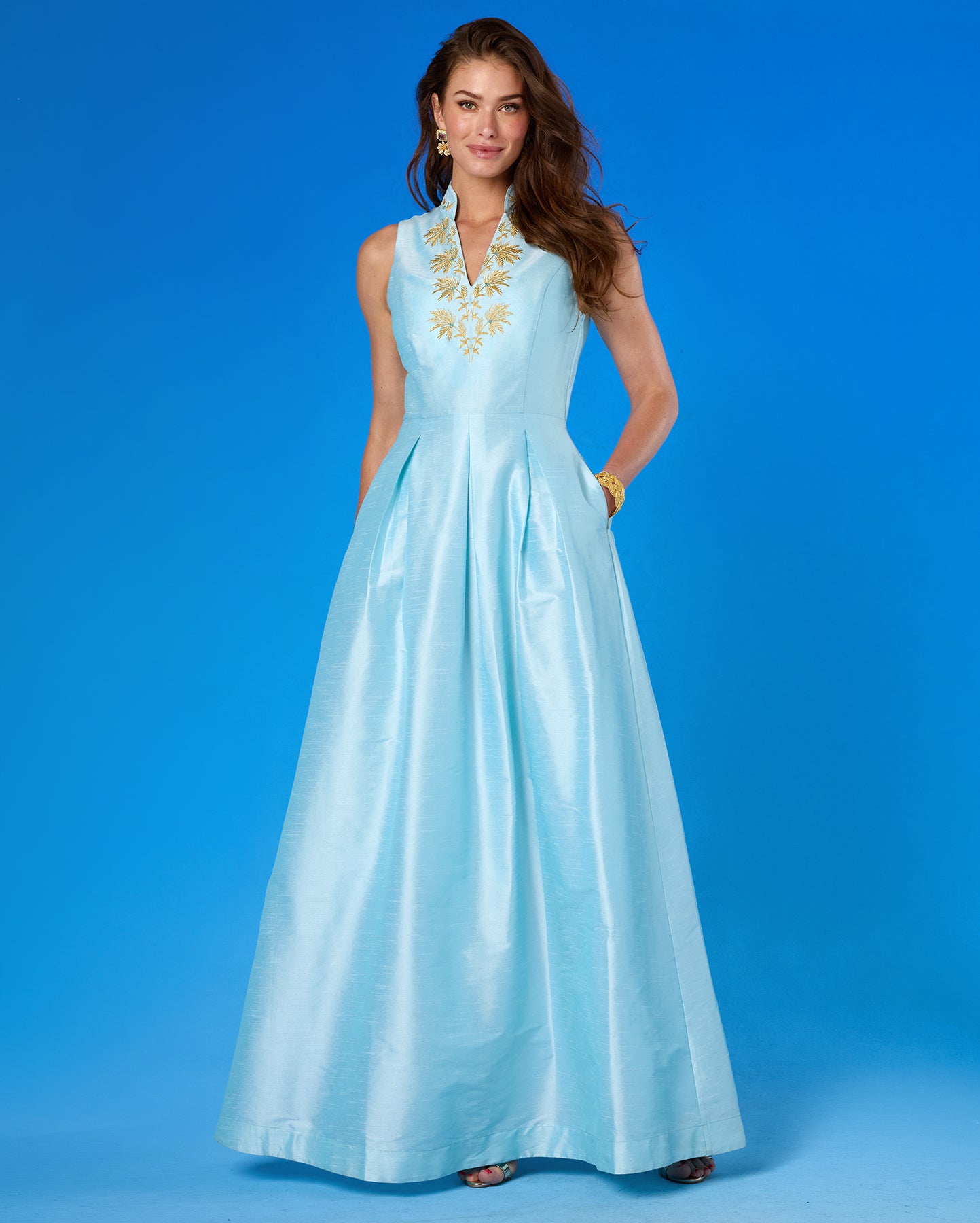 Woman wearing a light blue dress with gold embroidery against a blue background