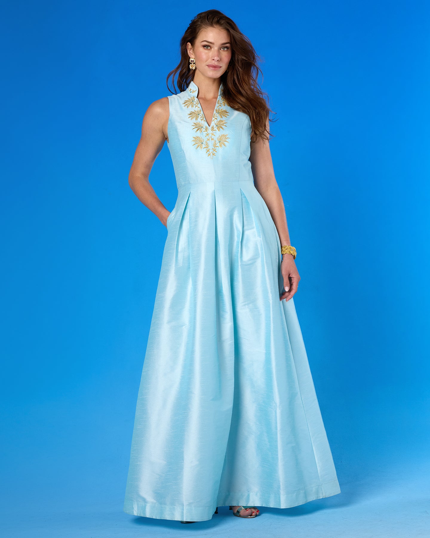 Woman wearing a light blue dress with gold embroidery on a blue background