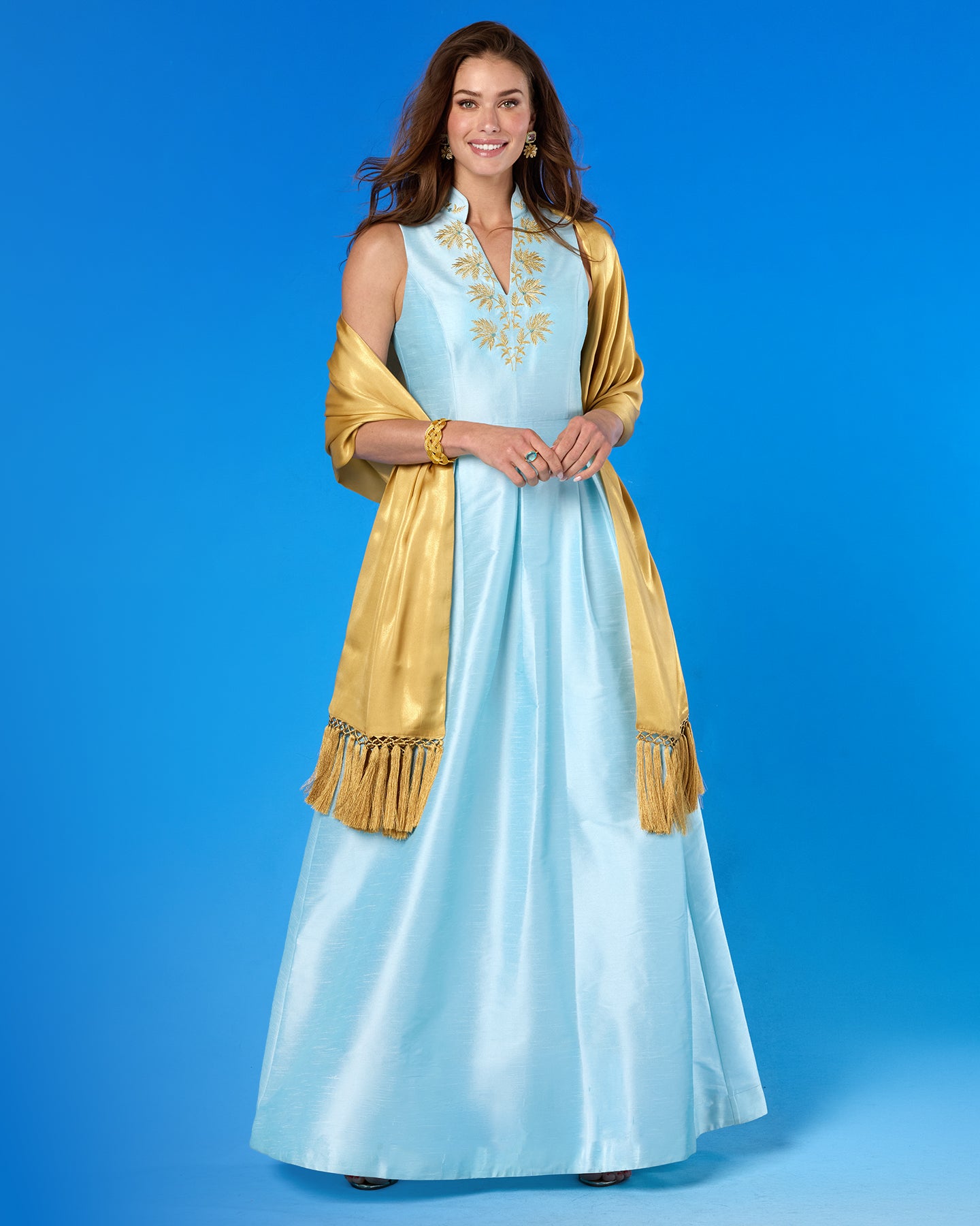 Woman wearing a light blue dress with gold accents against a blue background