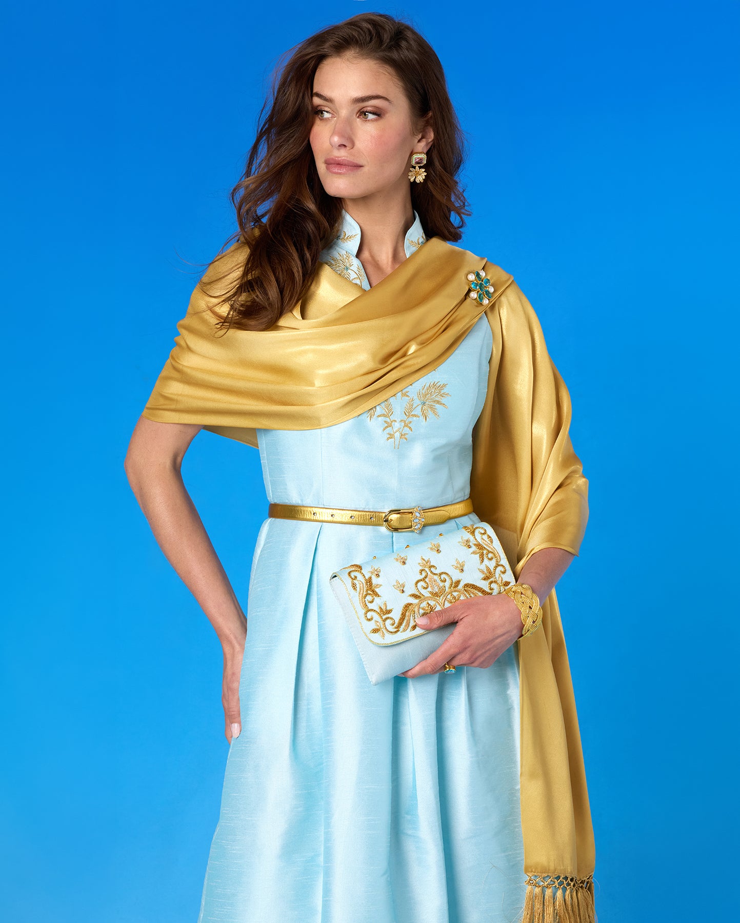 Woman wearing a light blue dress with gold accents against a blue background