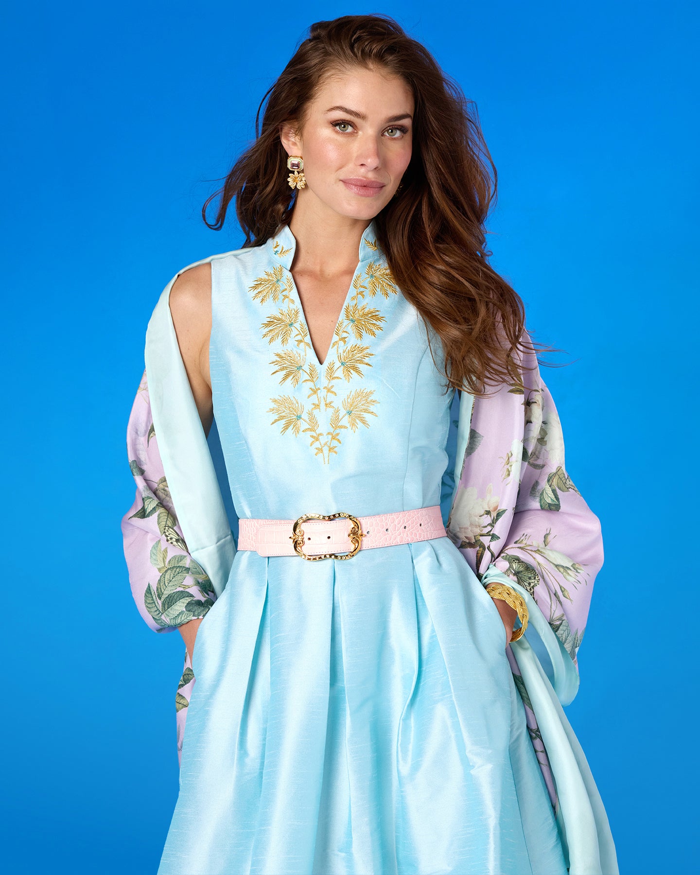 Woman wearing a light blue dress with floral embroidery against a blue background
